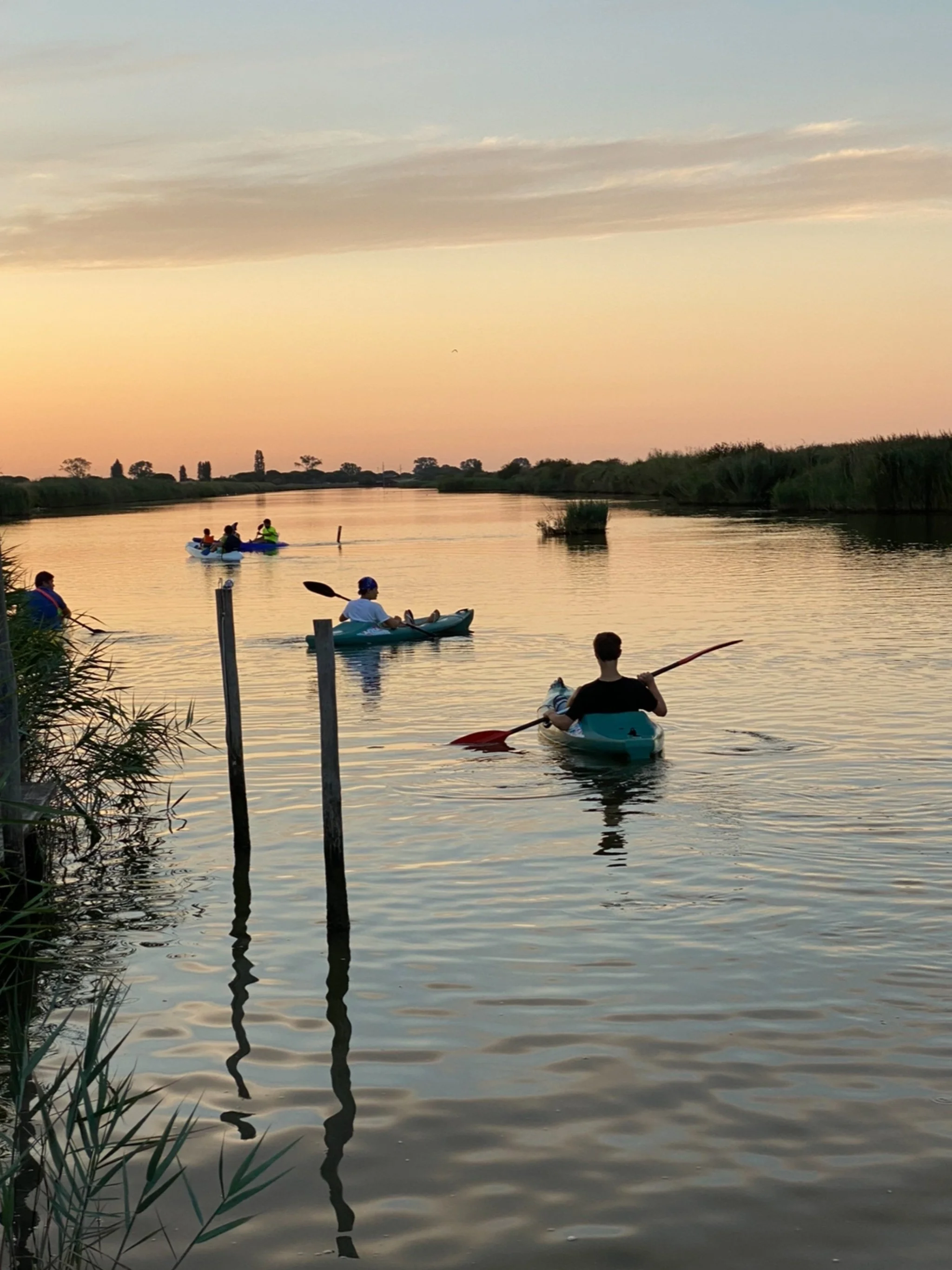 People kayaking on a calm river during sunset with pastel sky colors and reflections in the water.