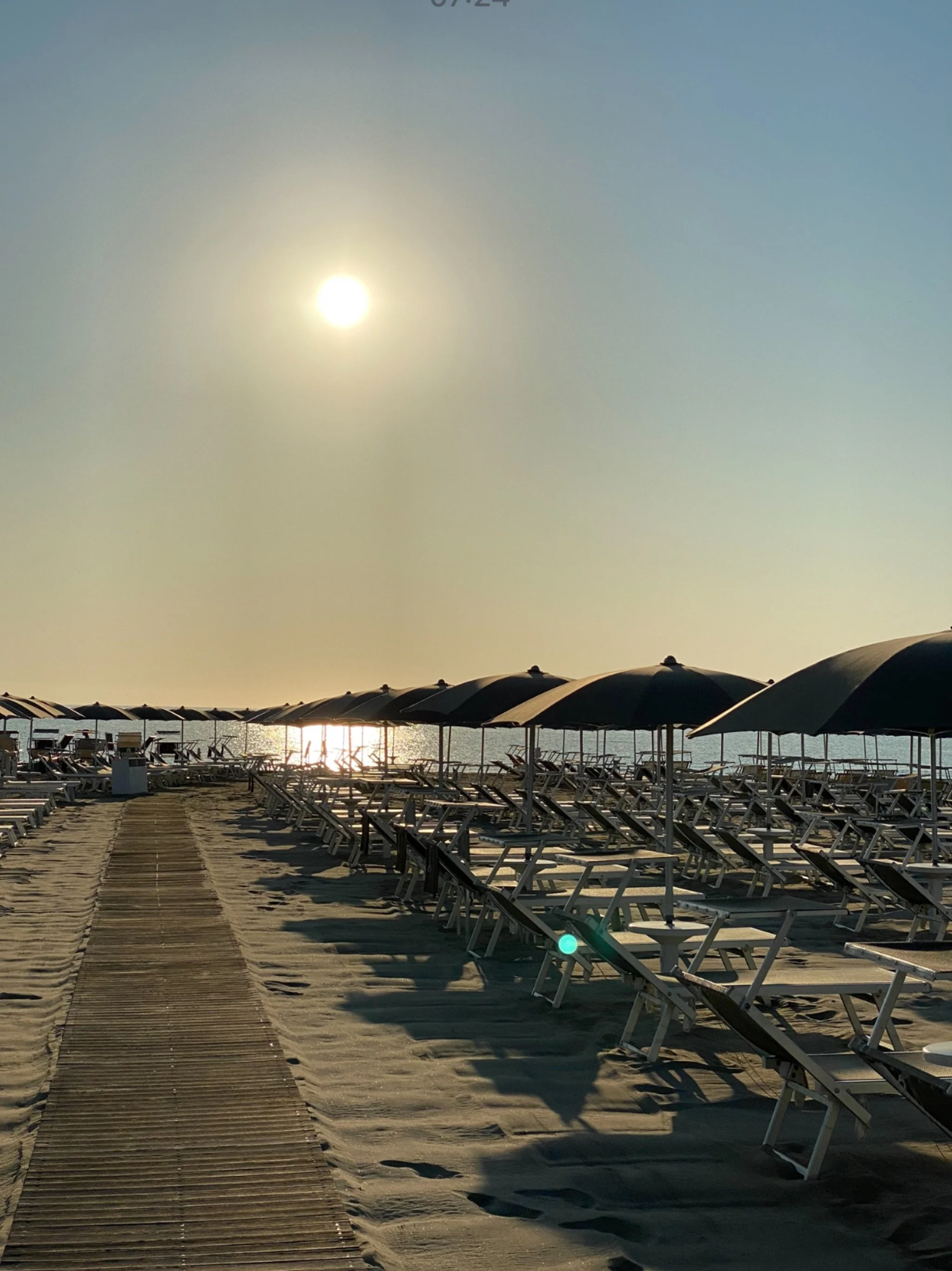 Empty beach with rows of lounge chairs and umbrellas during sunset or sunrise.