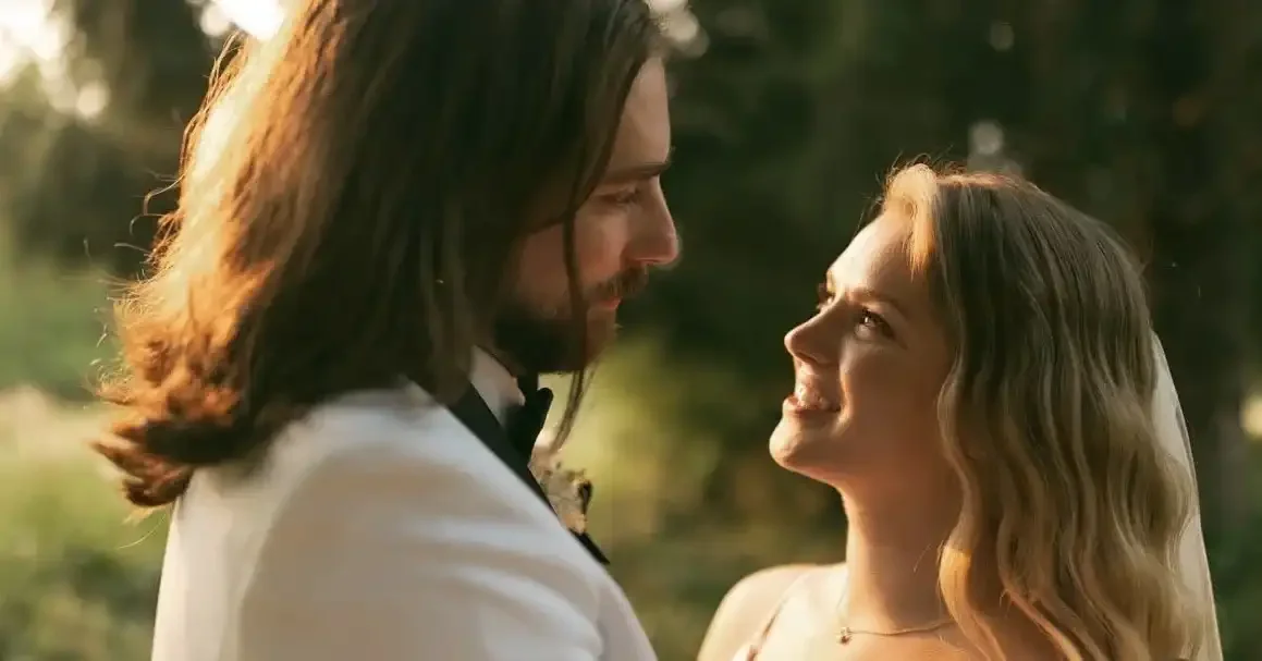 A bride and groom looking into each other's eyes during their wedding ceremony outdoors at sunset.
