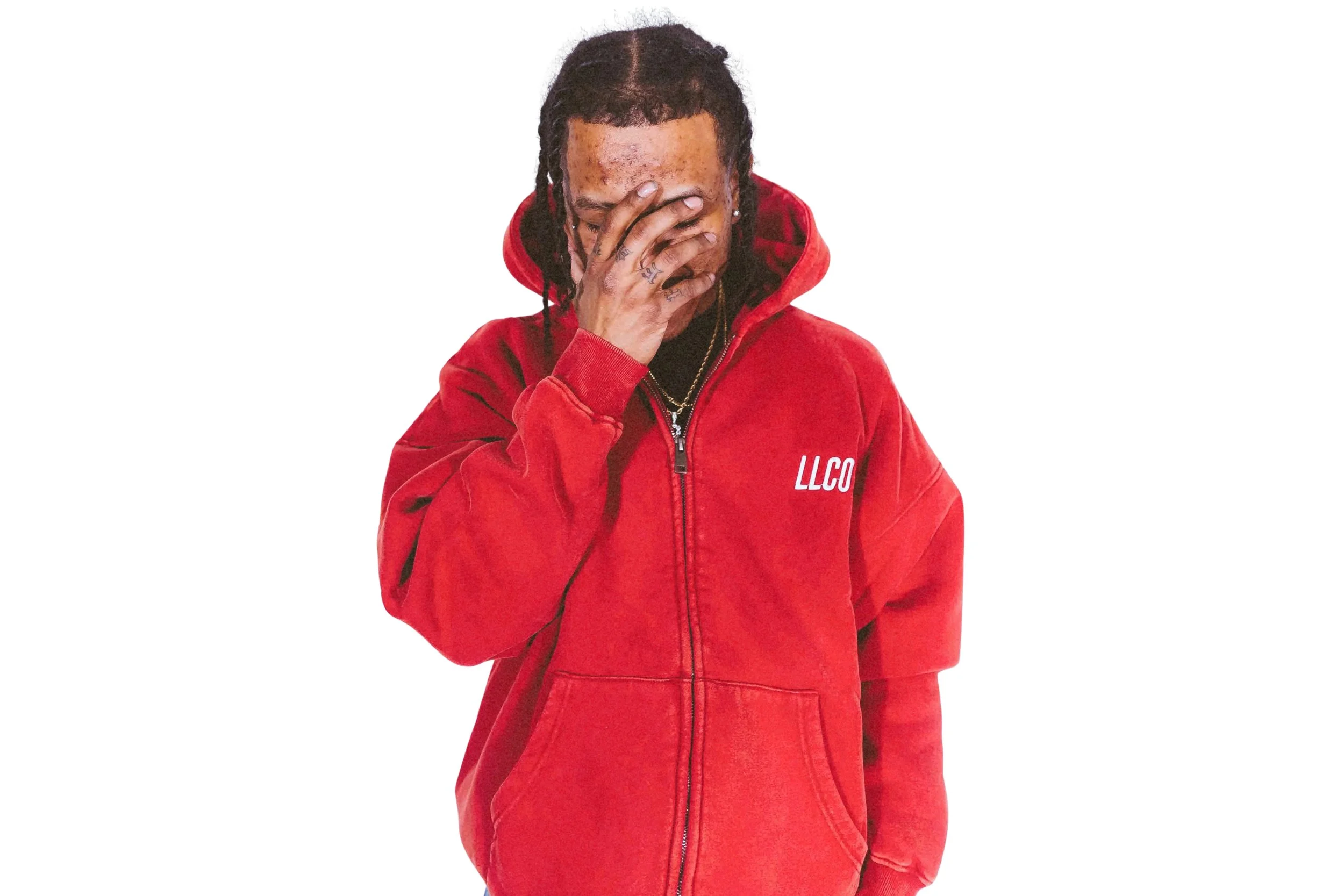 Person wearing a red LLCO hoodie with their hand covering part of their face, with visible tattoos on their fingers and bracelets, against a white background.