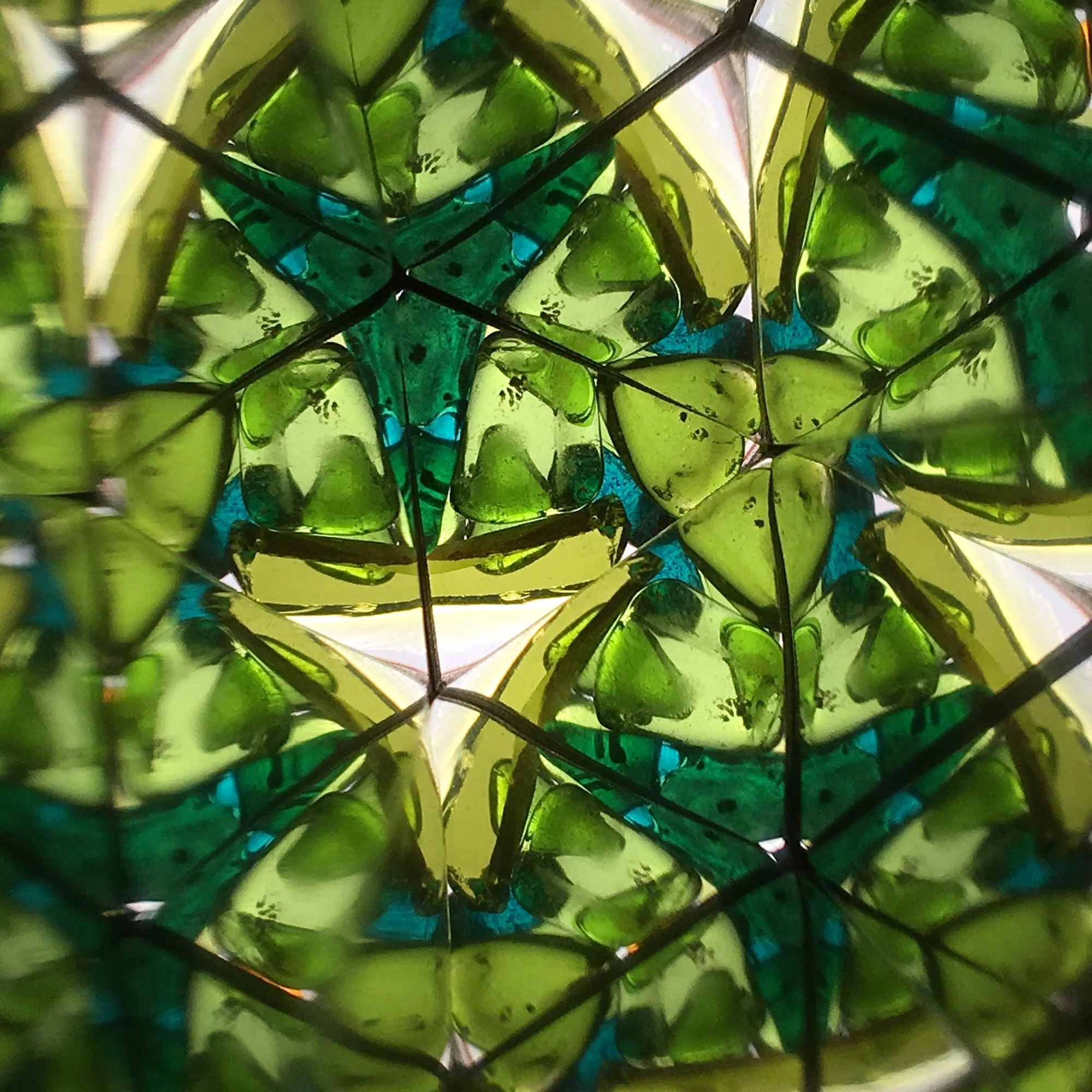 Symmetrical forest geometry with green and amber glass shards through a kaleidoscope.