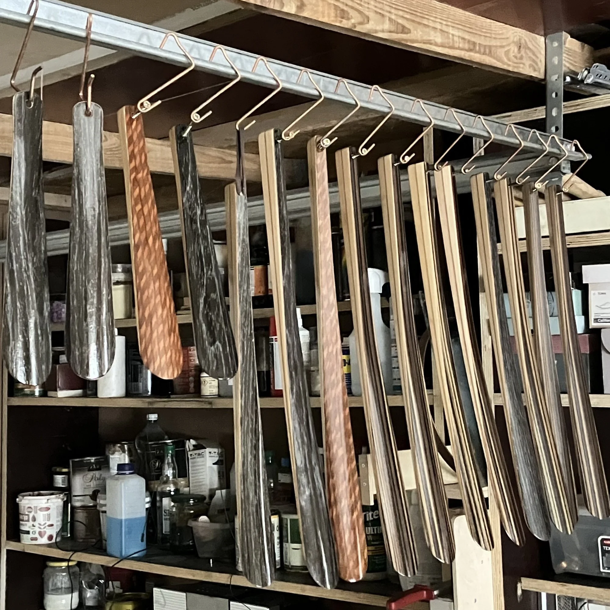  A row of handcrafted long wooden shoehorns in Black Oak, Zebrano, and Lacewood hanging in a workshop. 