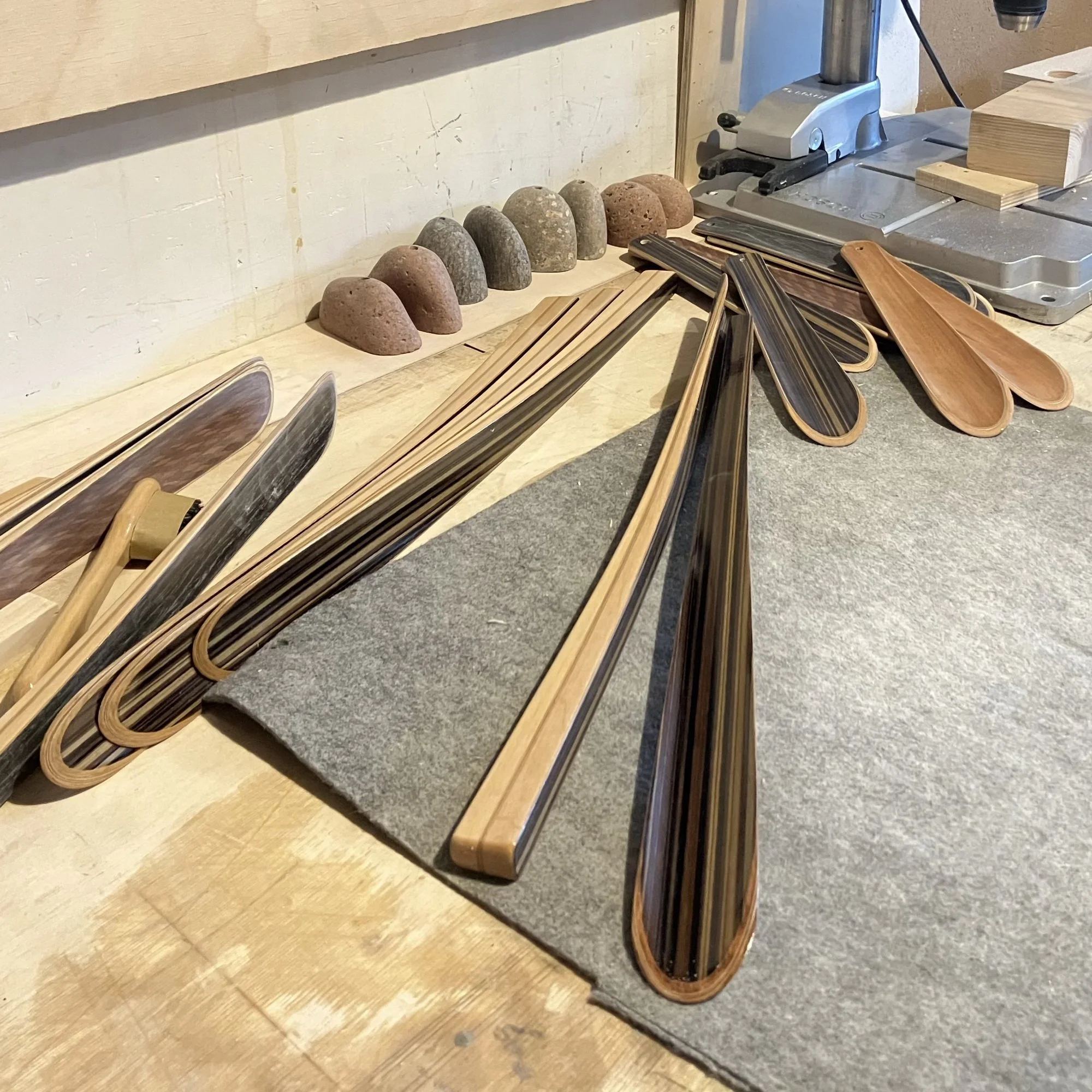 Finished wooden shoehorns laid out on a craftsman's workbench showing different wood grains and ergonomic shapes. 