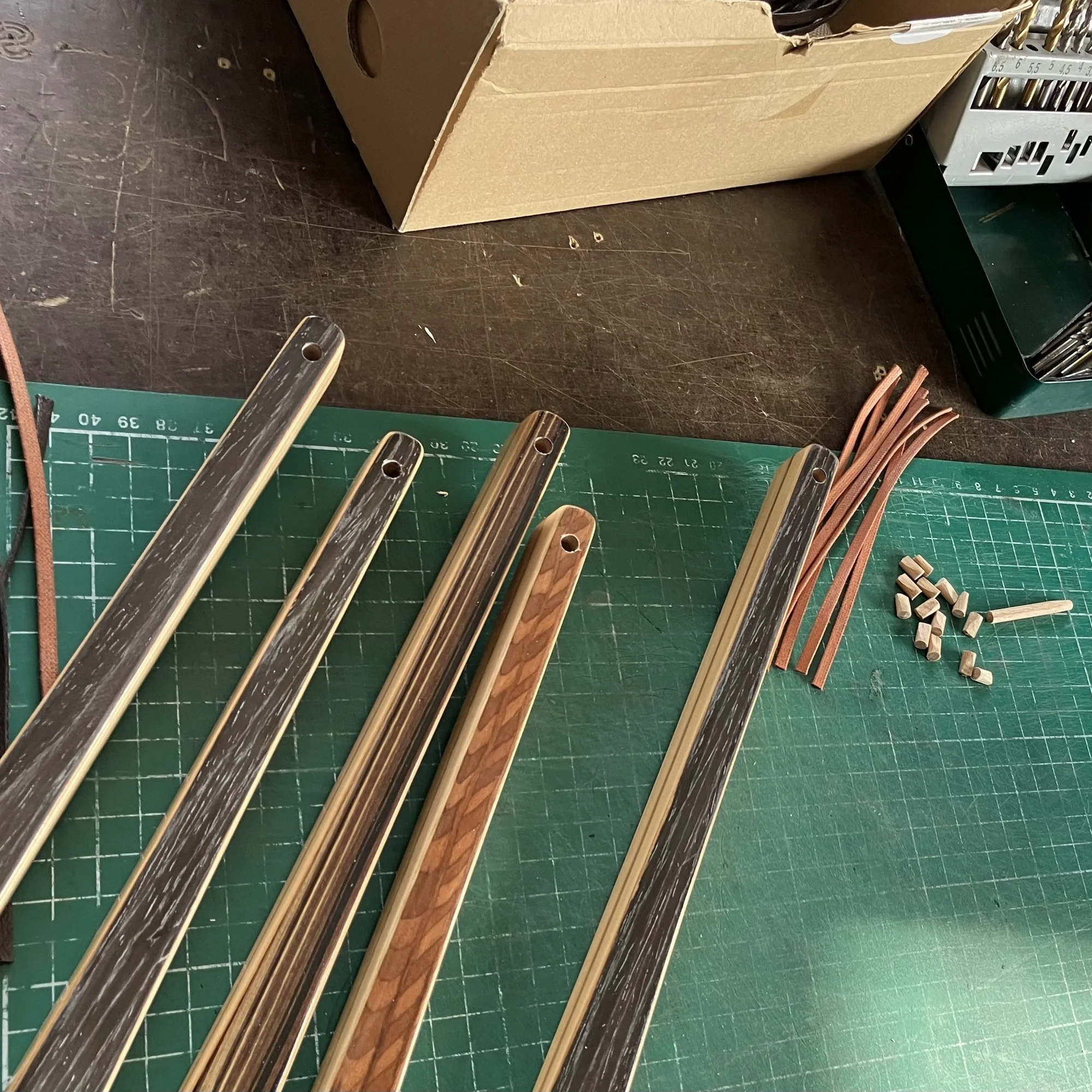  Close-up of Zebrano and Cherry wood shoehorns on a cutting mat with leather straps ready for final assembly. 