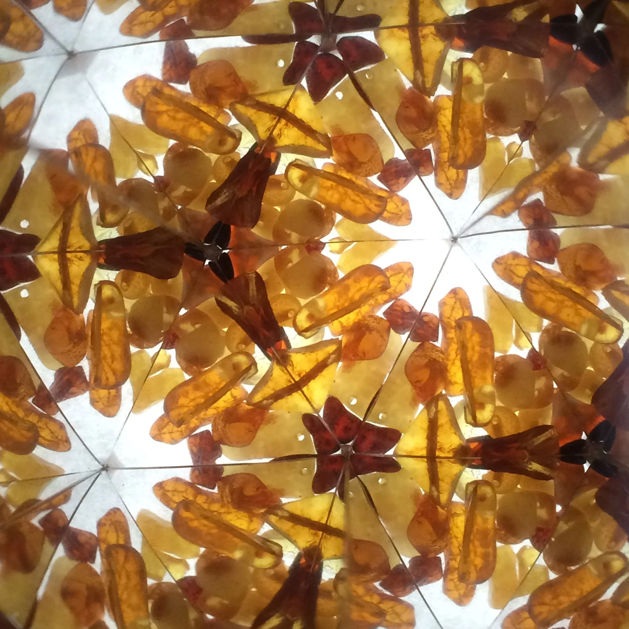  Geometric kaleidoscope pattern created from warm orange and dark brown amber pieces with soft light shining through the gaps. 