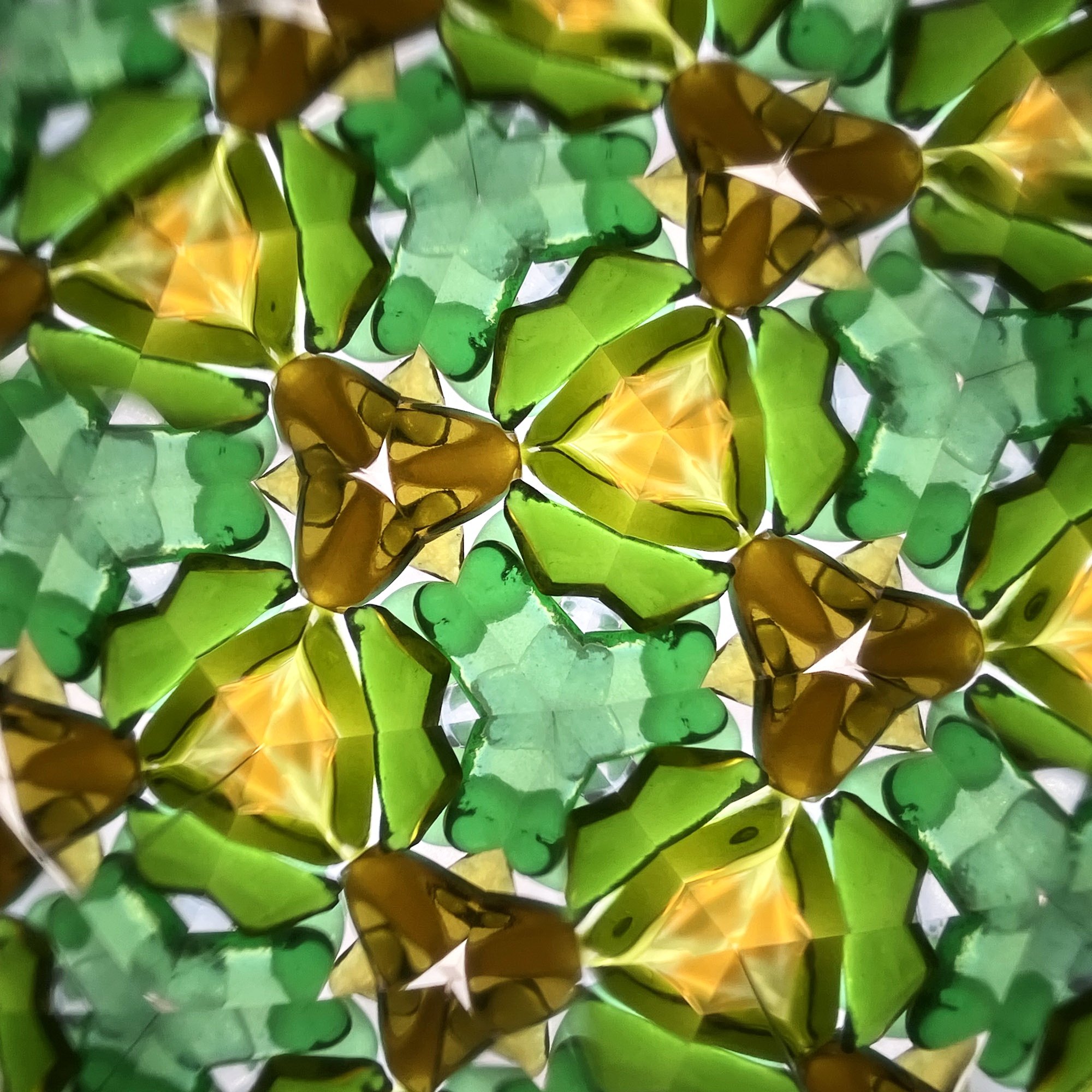  Symmetrical mosaic of emerald green and warm amber glass textures in a kaleidoscope format. 