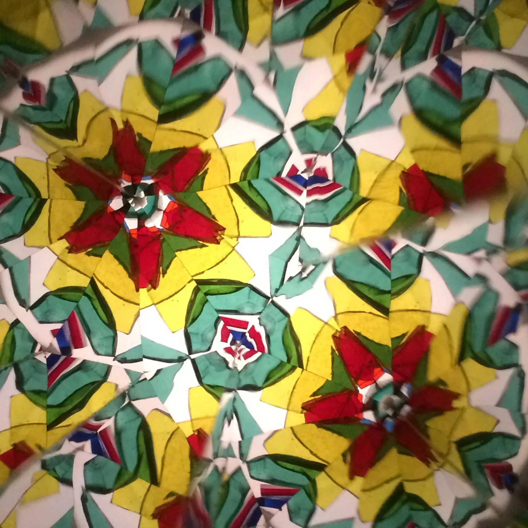  Intricate glass flower mandala featuring yellow star-shaped petals with red centers, outlined by emerald green glass fragments. 