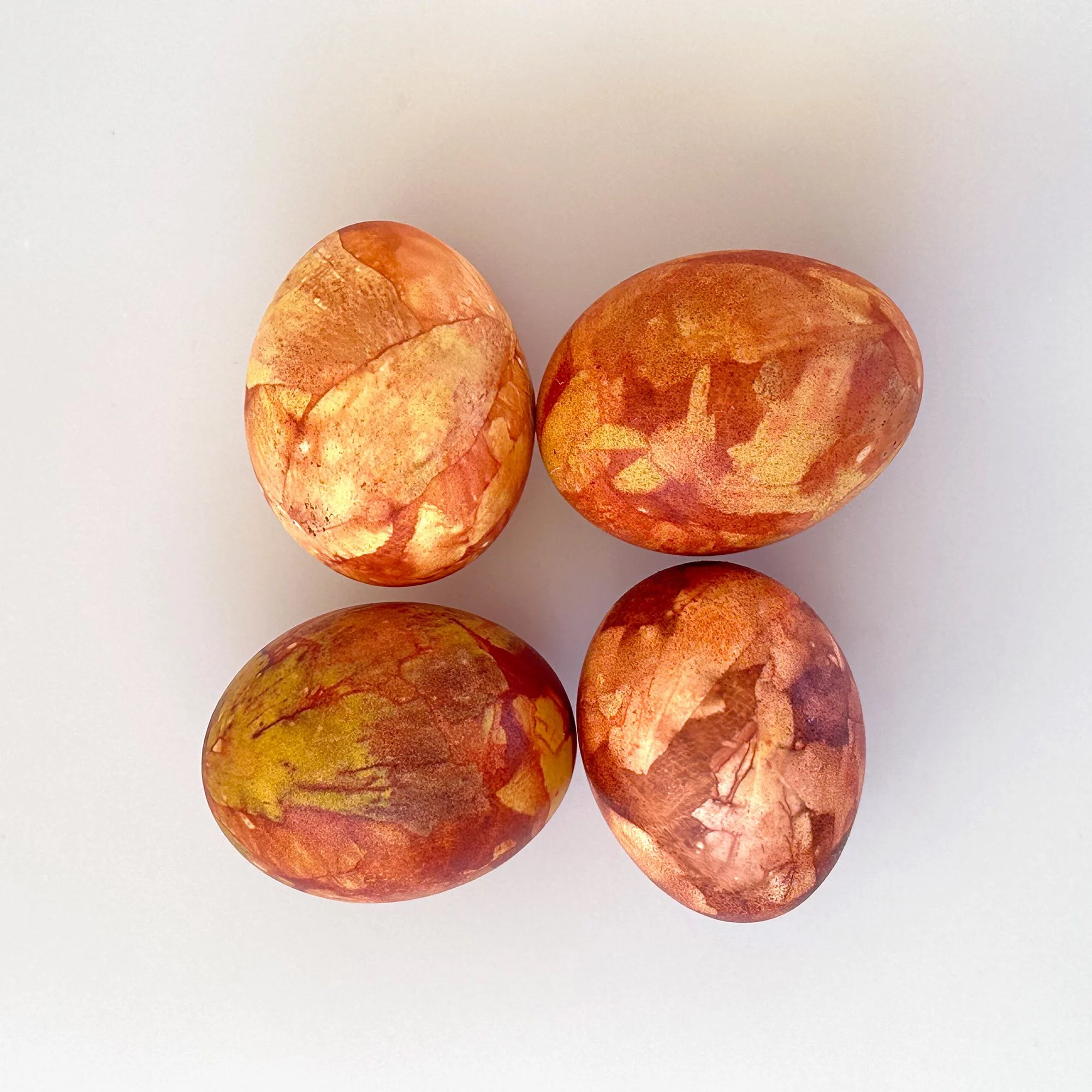  Easter eggs naturally dyed with onion skins, showing rich marbled textures in brown, orange, and amber tones on a white background. 