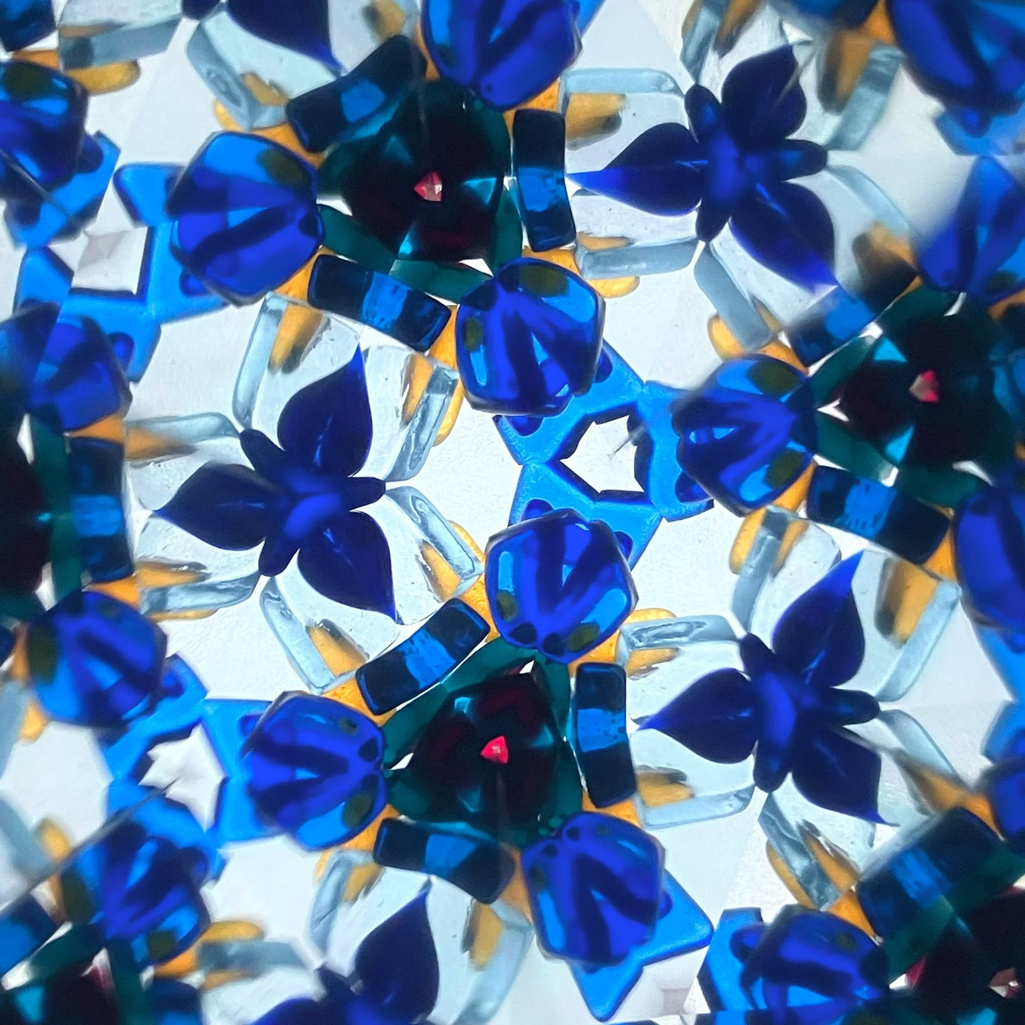  Blue kaleidoscope mandala with floral geometric symmetry, resembling Moorish ornament patterns with deep sapphire glass and repeating radial structure. 