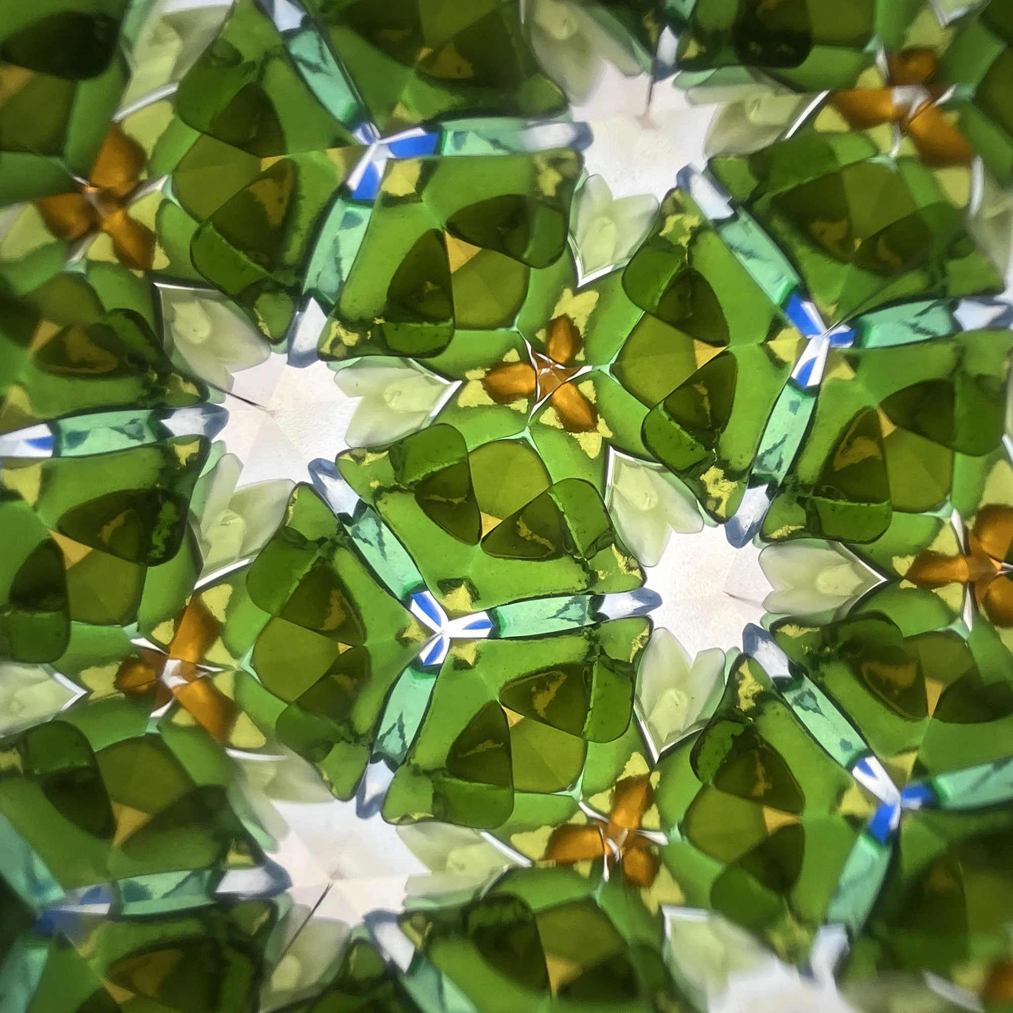  Symmetrical kaleidoscope pattern made from recycled bottle glass, featuring deep forest green and bright white star-like shapes. 