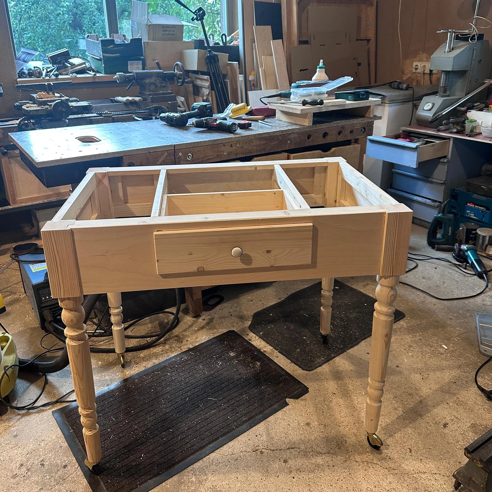  Wooden desk skeleton with a central drawer installed, standing in a workshop environment. 