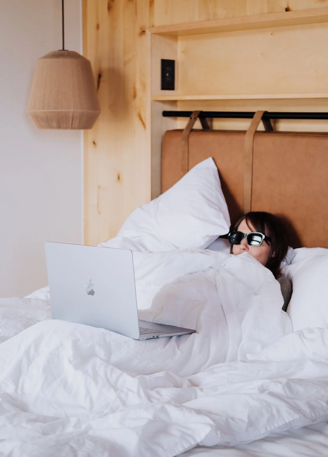 A woman lays with her laptop in a hotel bed