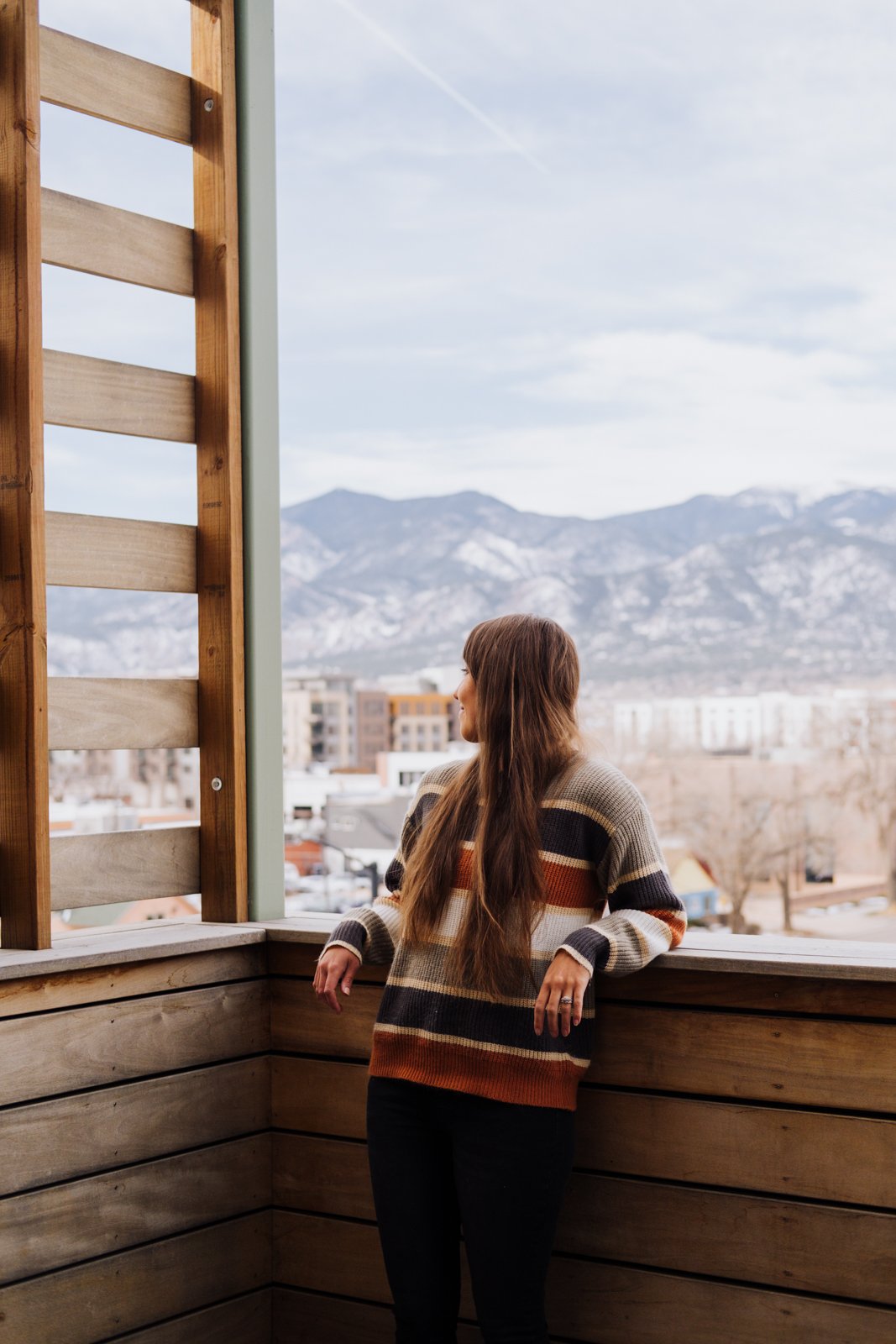 A woman stands on a balcony with the Rocky Mountains behind her