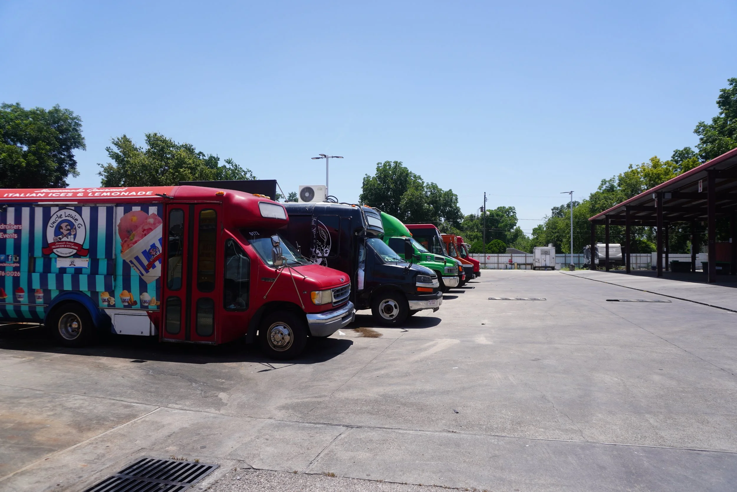 Parking lot with food trucks and trees in the background under a clear blue sky.