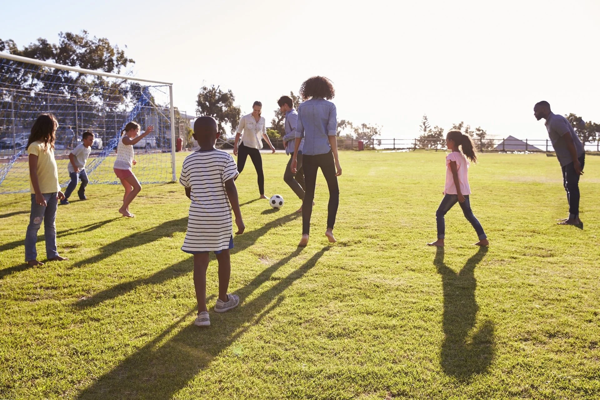 Families and children playing soccer together on a sunny day in the park.