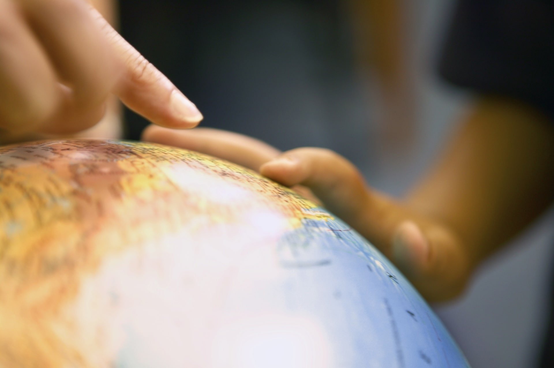 Close-up of hands pointing at locations on a globe during a geography activity.
