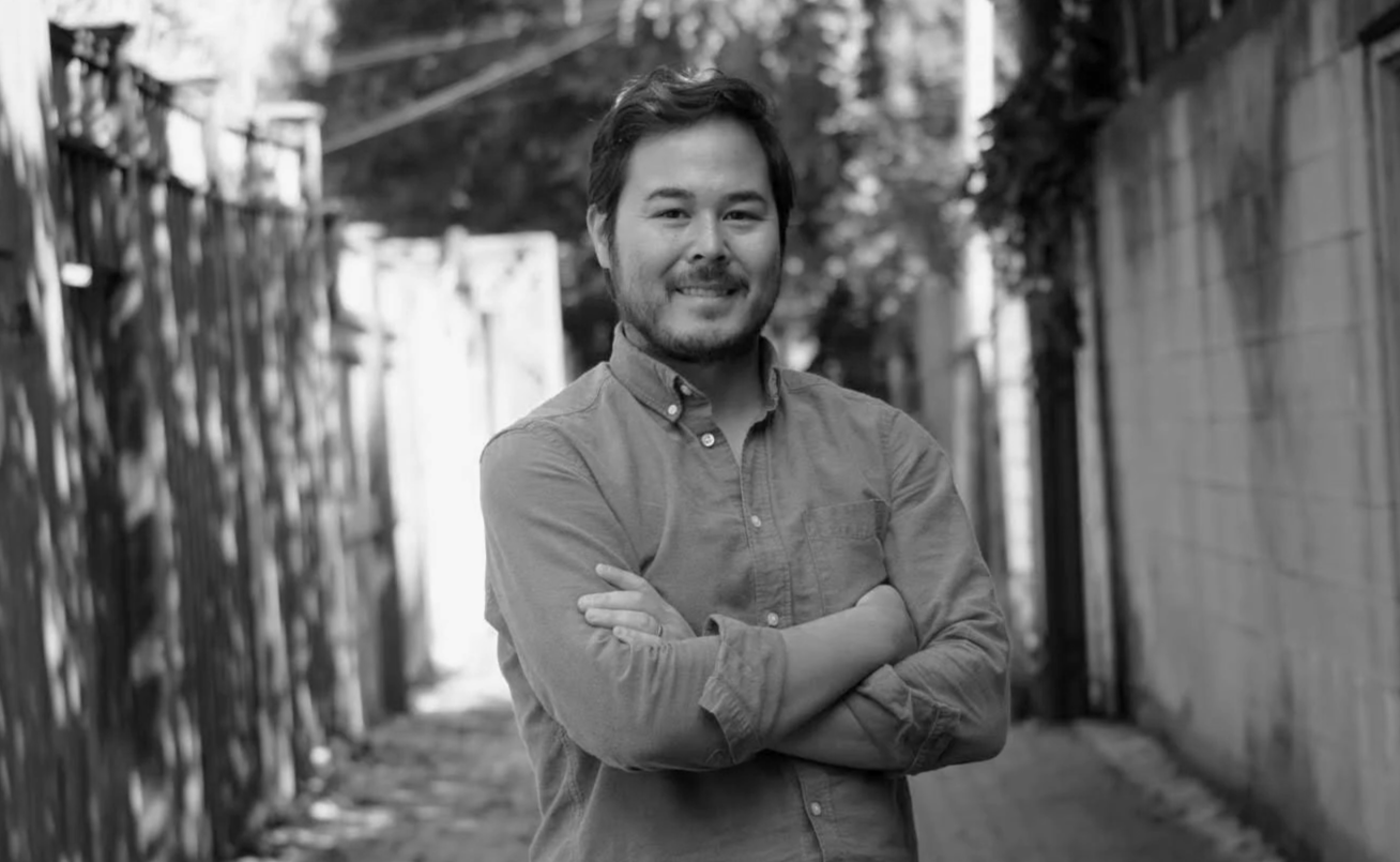 The founder of Aki, a mid-thirties male, smiling with his arms crossed in a professional portrait using a natural setting as a background.