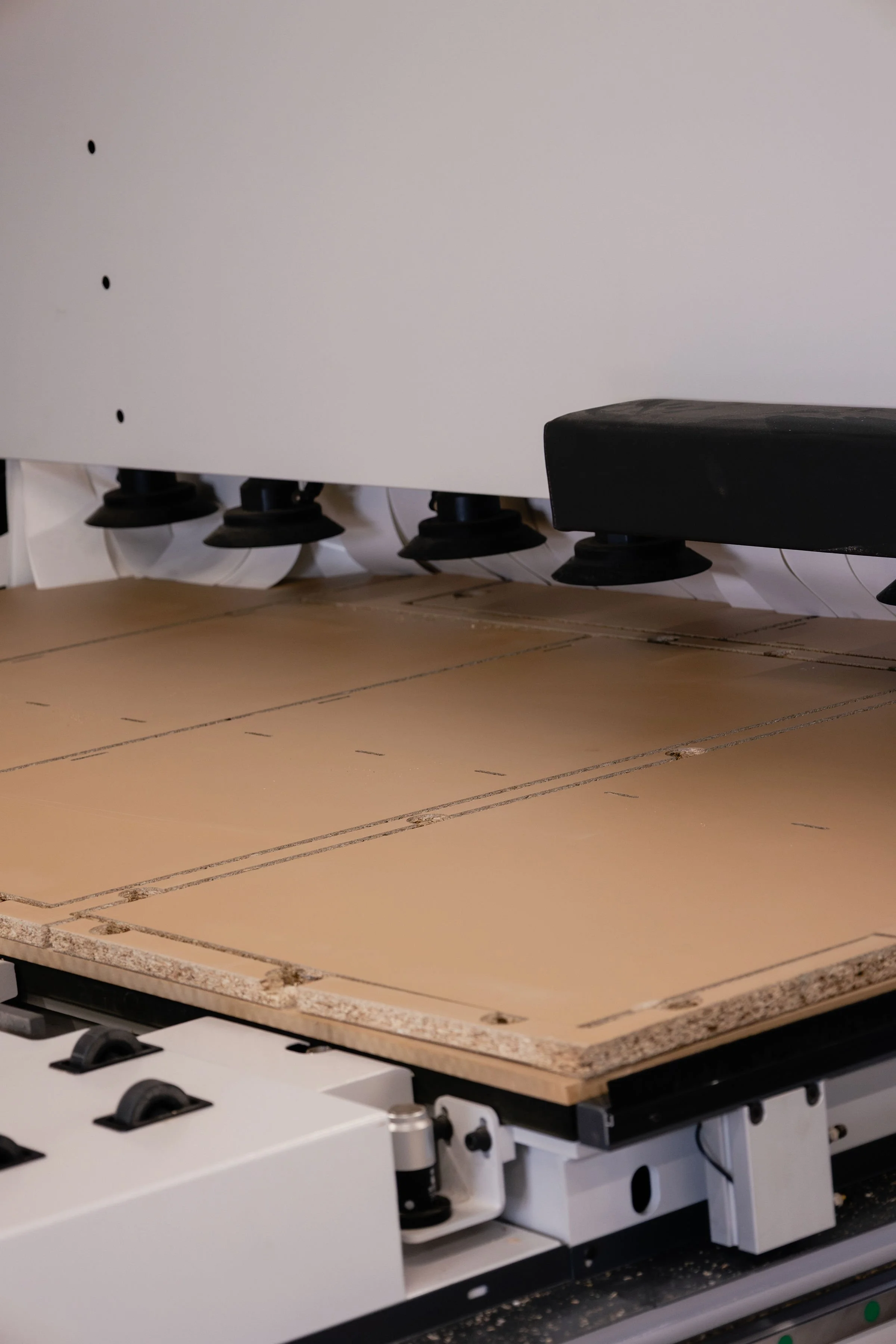Close-up of a CNC machine cutting a piece of wood or particleboard with visible chips and cut lines.