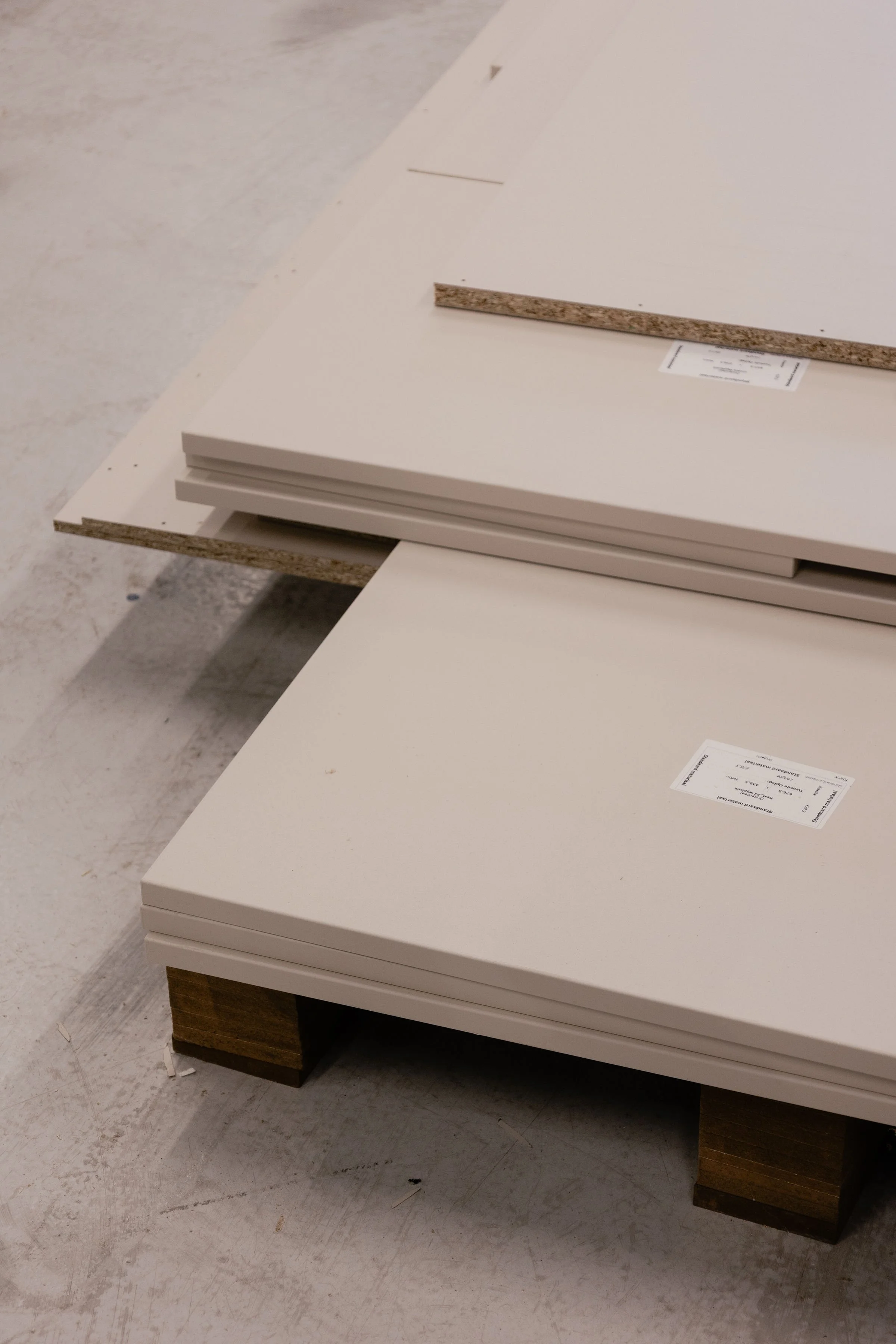 Close-up of a white cabinet or drawer unit placed on a wooden stand in an unfinished indoor space with concrete floor.