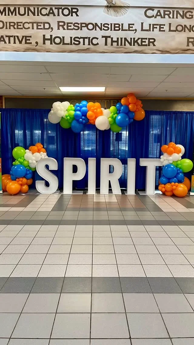 Decorative display spelling 'SPIRIT' with colorful balloons and blue curtains in the background.