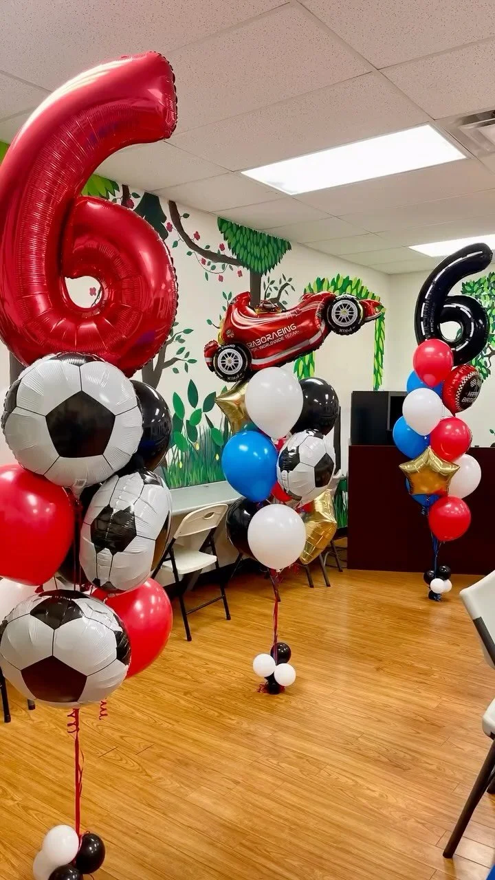 Decorations for a child's sixth birthday party with red, white, black, and blue balloons, including soccer ball themed balloons, and a red race car-shaped balloon.