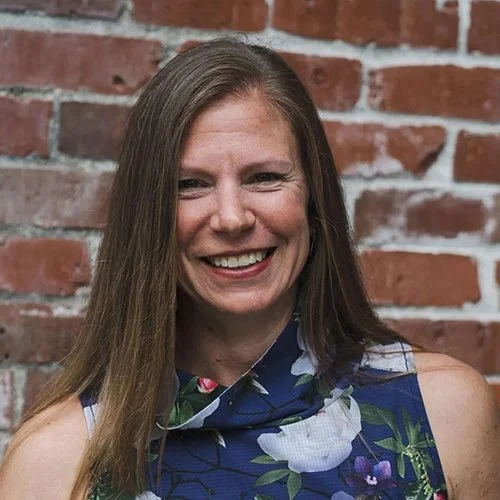 Beth with long, light brown hair in a blue floral shirt smiles at the camera