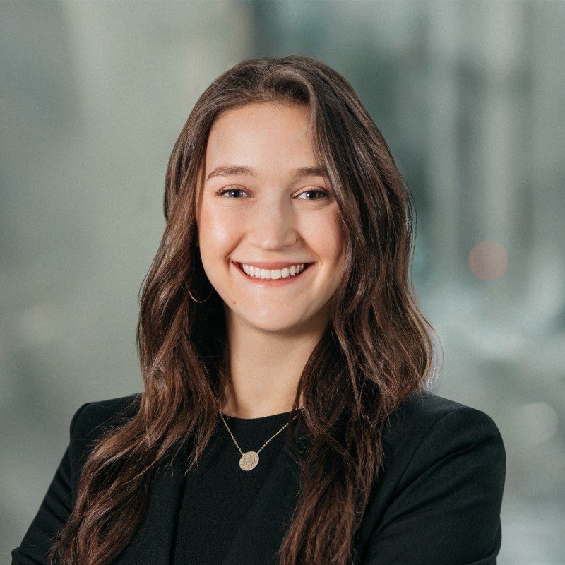 Marissa with long, brown, wavy hair, and black blouse, and pendant necklace smiles at the camera.
