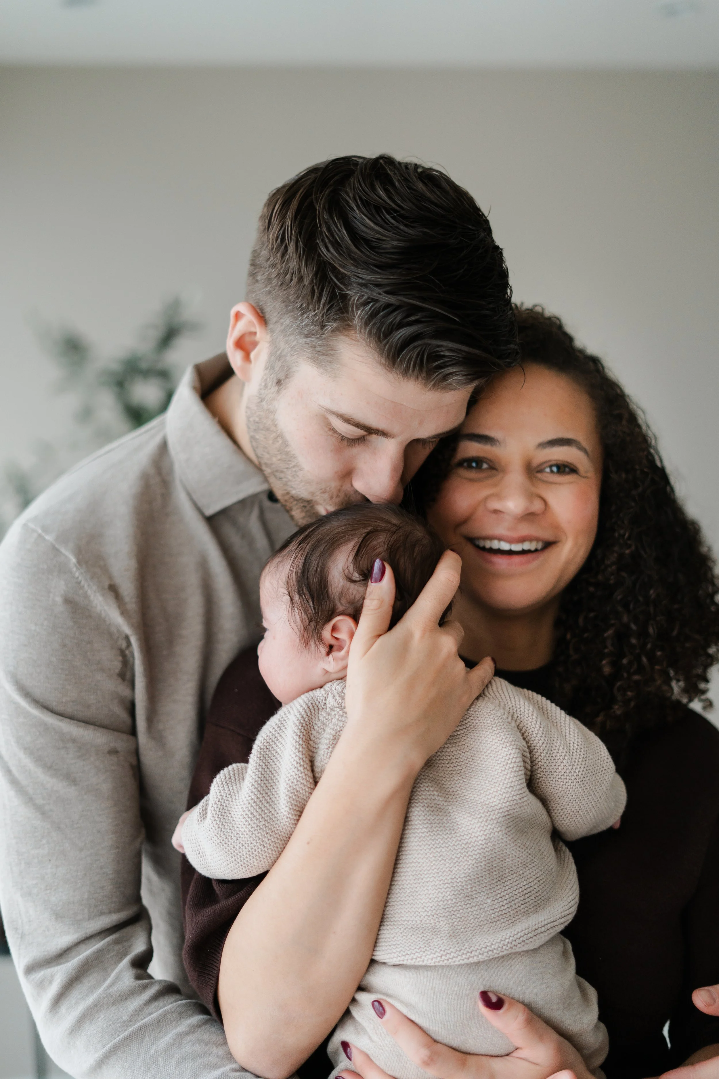 Een gelukkige familie met een man, vrouw en baby die samen kusjes en knuffels geven.