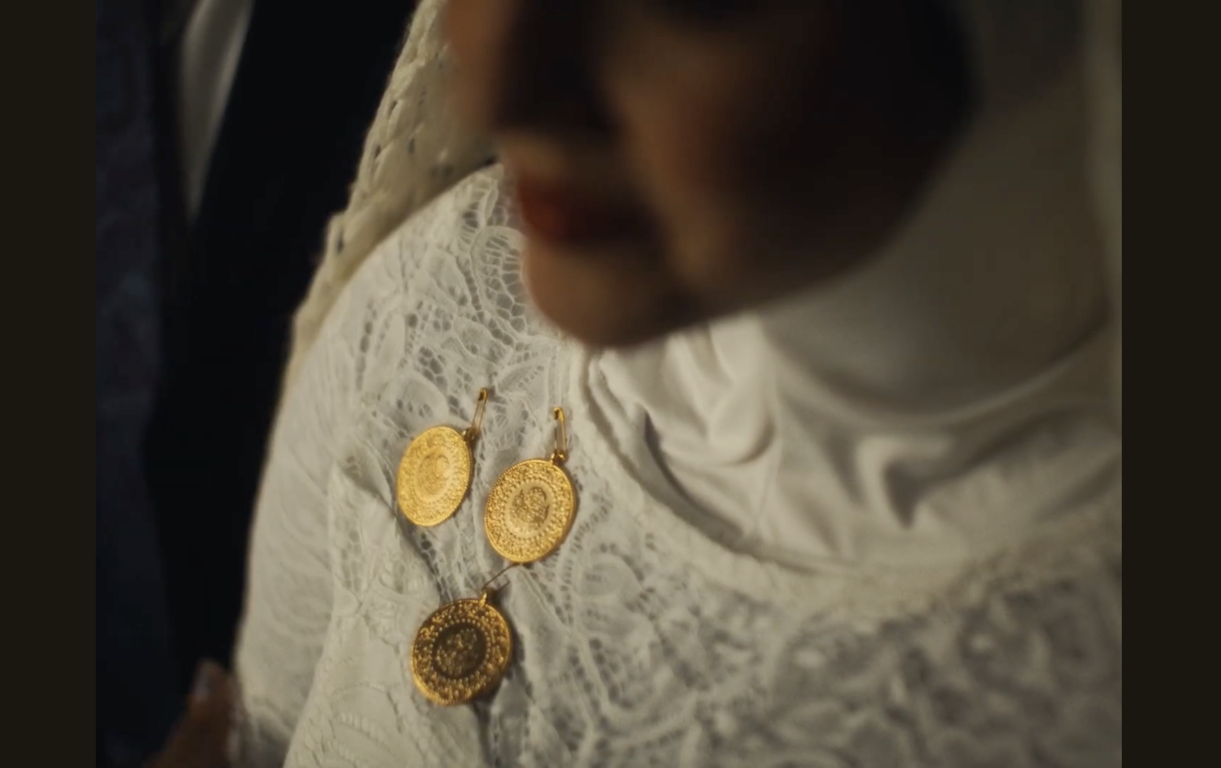Close-up of a person's chest wearing a white lace top and adorned with large gold circular coins.
