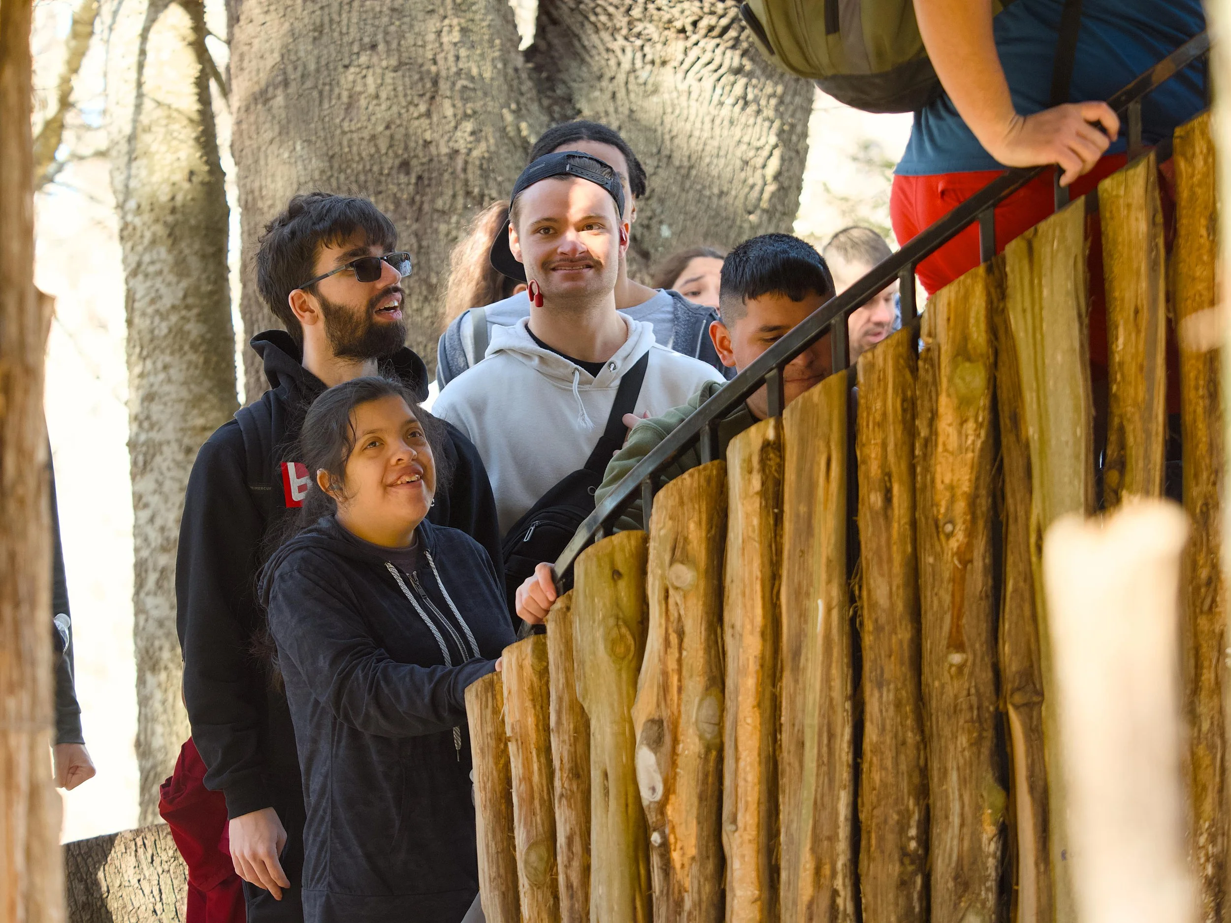 Group of people standing in line outdoors, with trees in the background, climbing up wooden stairs.