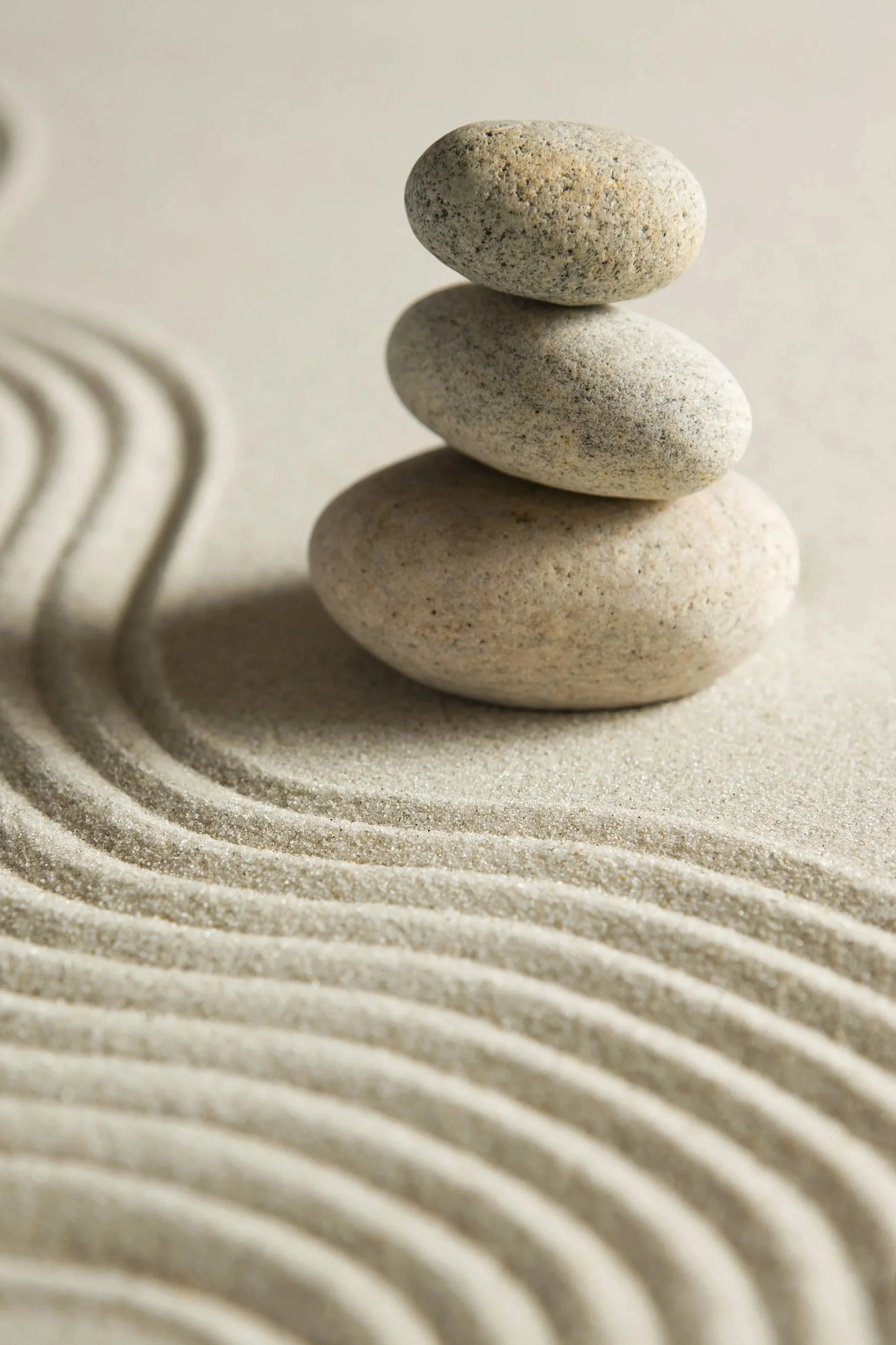 Three stacked smooth stones on sand with concentric ripples