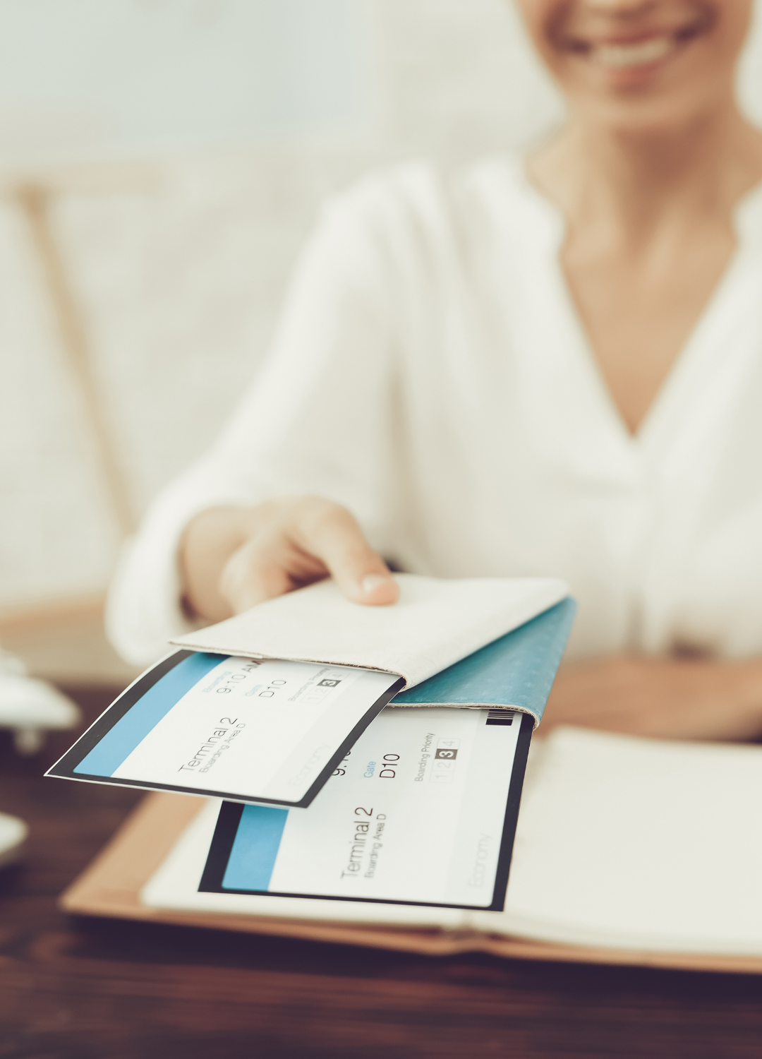 Person placing airline boarding passes into a blue passport cover on a wooden table.