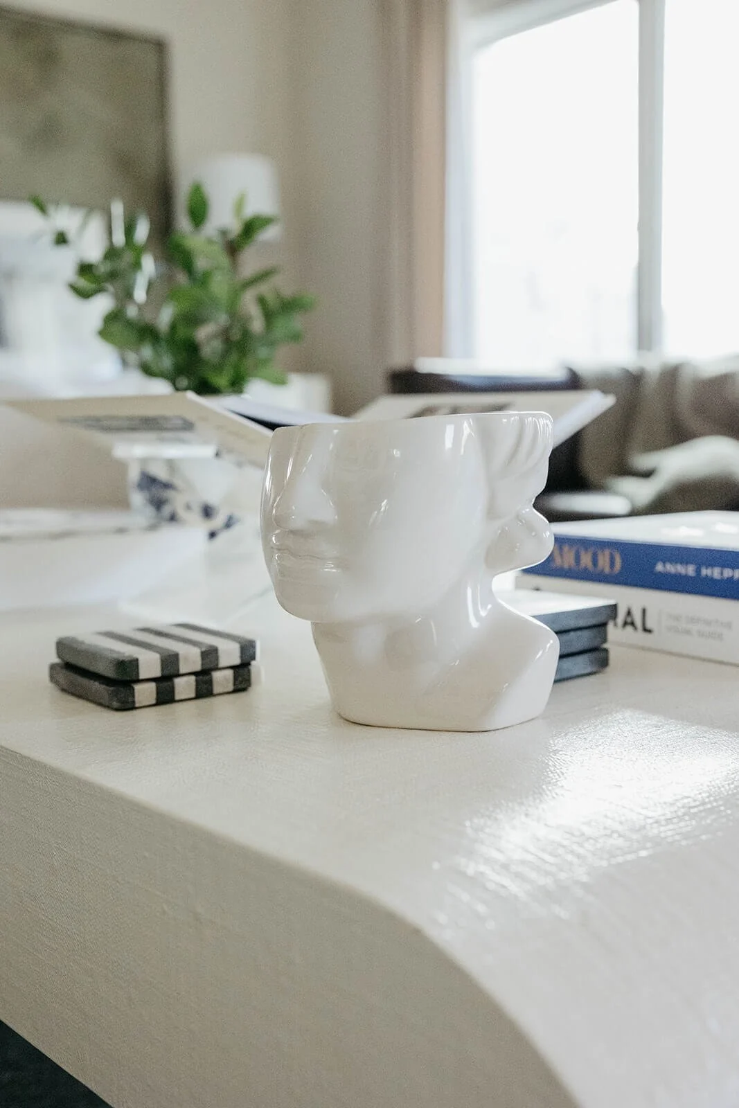 Close-up of the white coffee table featuring a unique white ceramic face sculpture and a stack of black and white striped coasters.