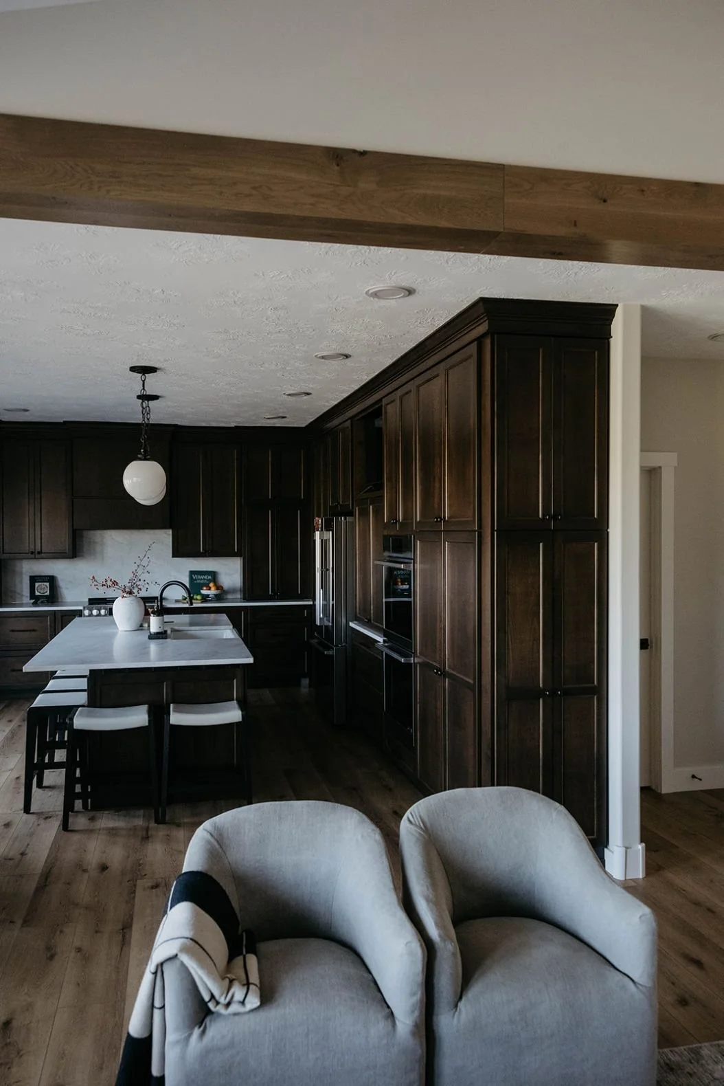 View of the spacious kitchen with rich, dark-stained wood cabinetry and a large white island. A light wood beam crosses the ceiling.