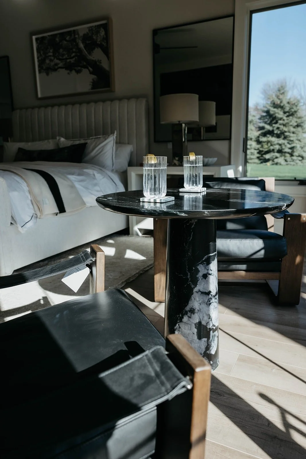 Master bedroom corner sitting area with a black marble pedestal table and black leather seating, offering a bright view through the sliding doors to the backyard.