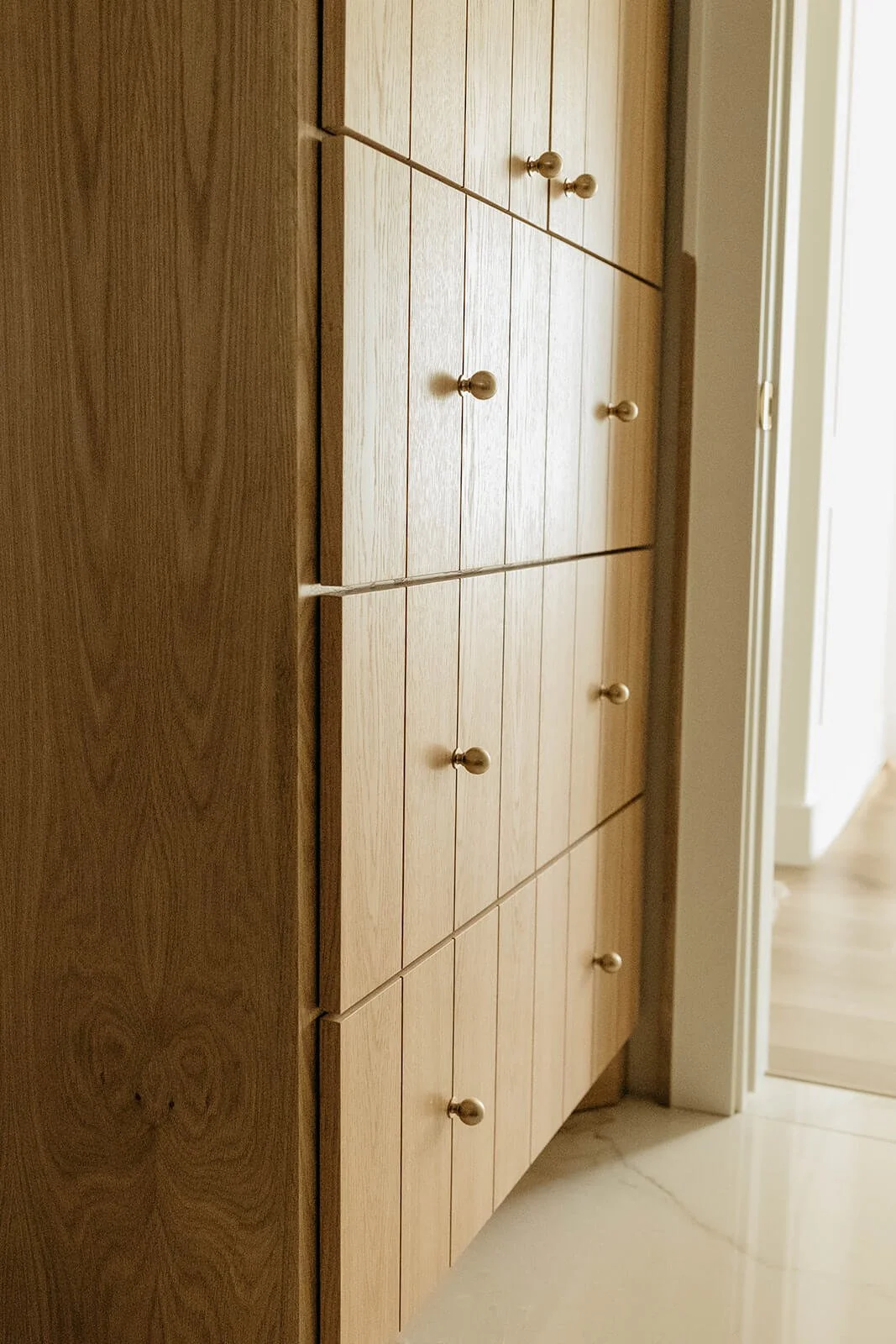 Close-up of the natural light wood vanity with tall, stacked drawers, emphasizing the vertical grain and small round brass knobs.
