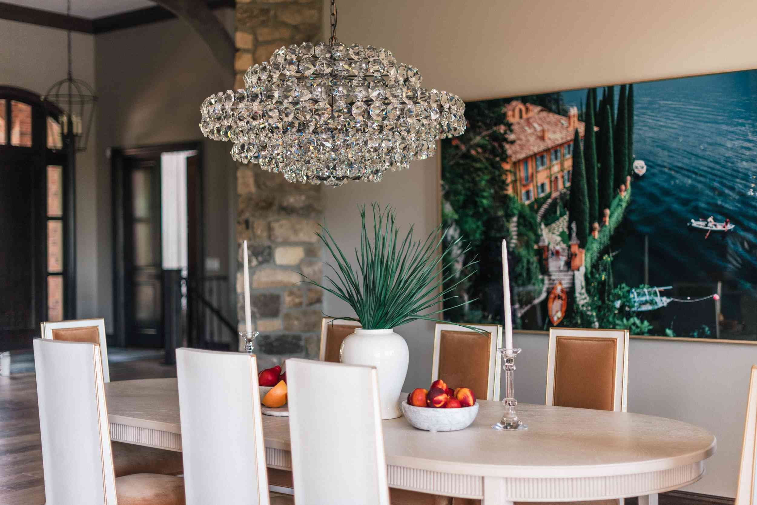 View of the cloud-shaped crystal chandelier hanging above the dining table, with an oversized modern print depicting water and land in the background.