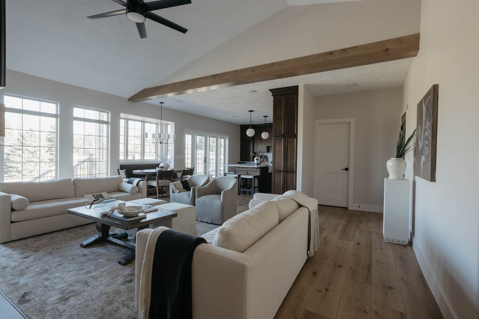 Expansive view of the living room featuring wood flooring, a large area rug, a fireplace, and a light-colored sectional, emphasizing the vaulted ceiling and beams.