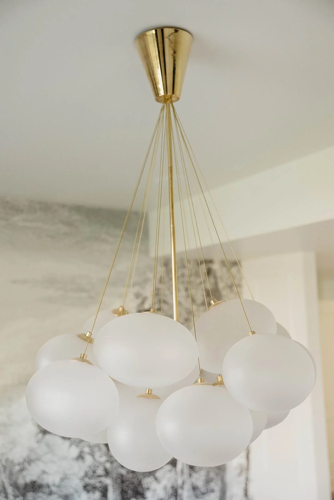 Close-up of a stunning modern chandelier with a gold canopy and multiple frosted white glass globe lights suspended by thin wires.