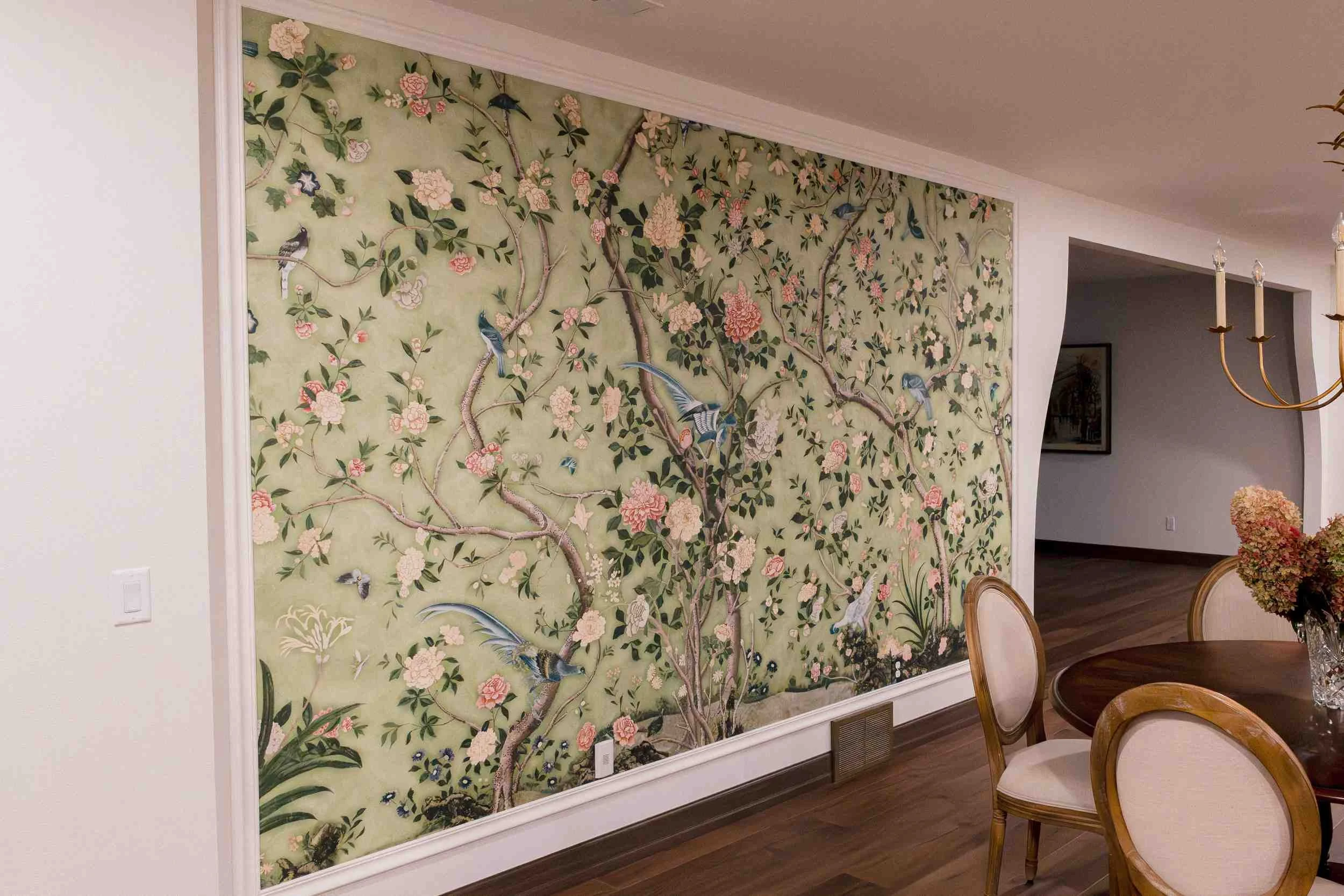 Dining room feature wall with light green chinoiserie wallpaper depicting birds and flowers, set above traditional white wainscoting.