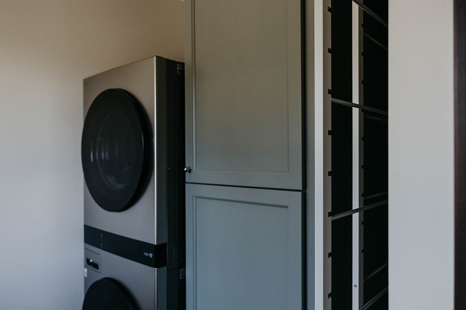 Low-angle view of the base of the stacked washer and dryer units, next to the tall utility cabinets.