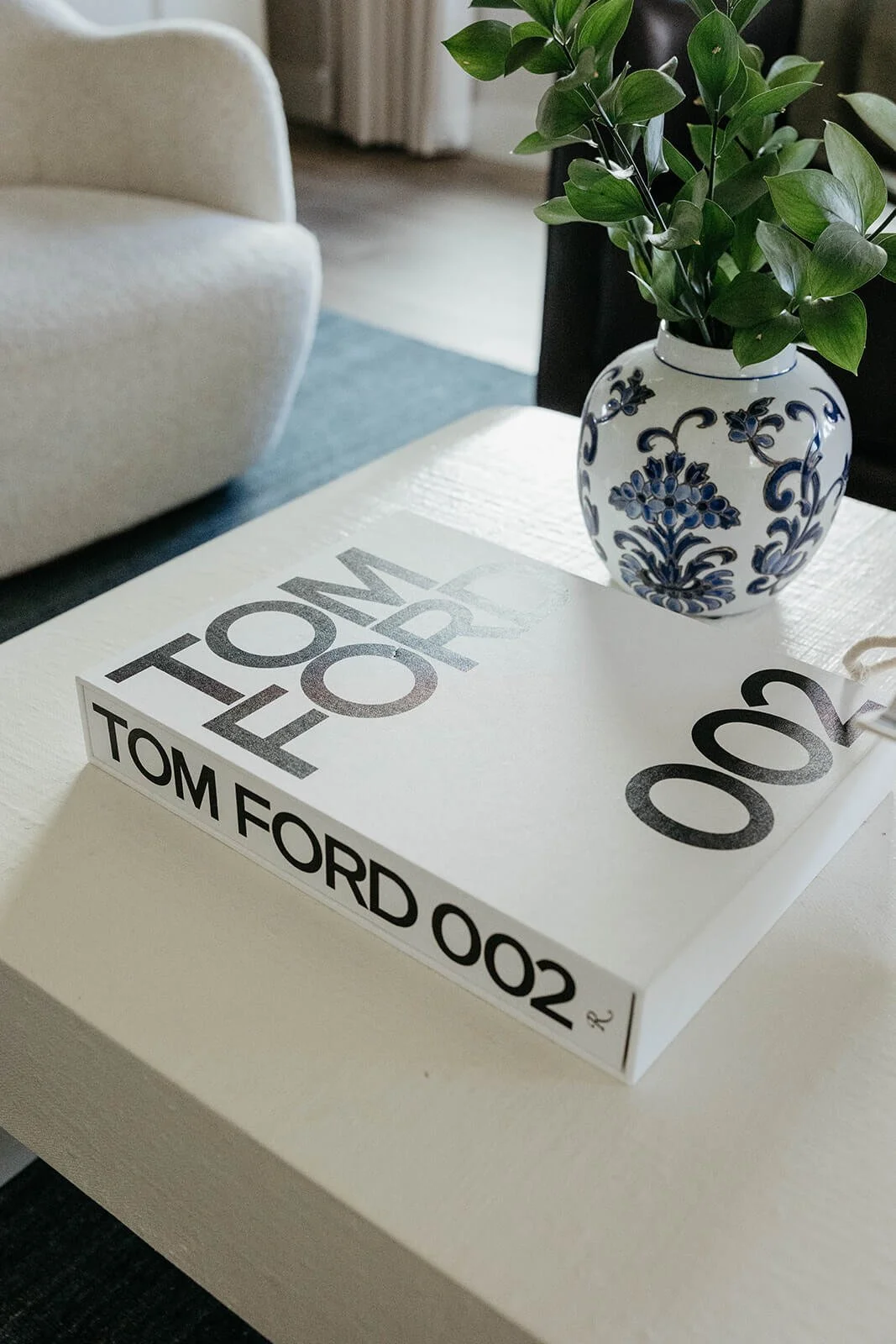 Close-up of a large white Tom Ford book on a white coffee table, next to a blue and white chinoiserie vase with fresh greenery.