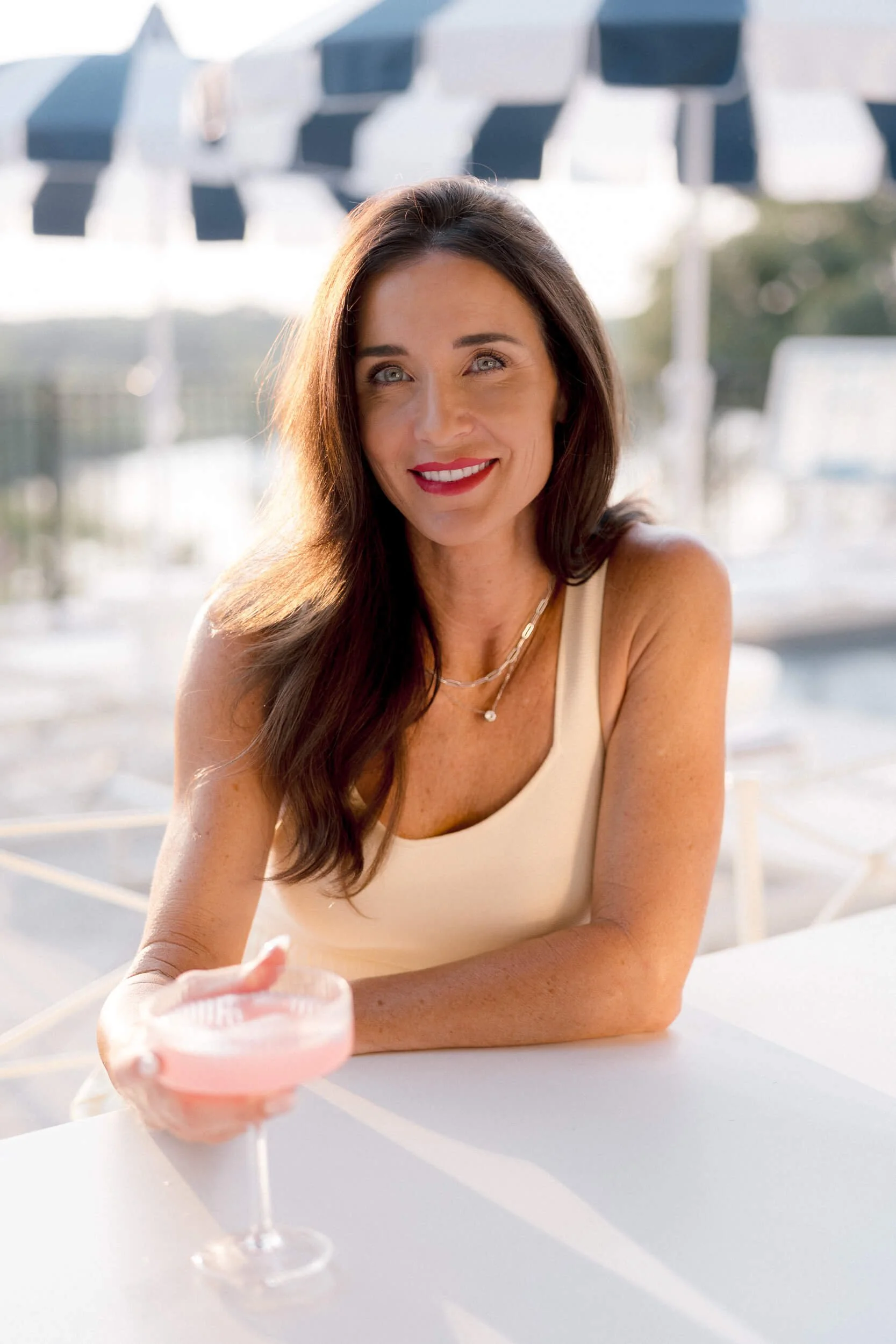 Christy Steen smiling while holding a glass of pink lemonade in her backyard. Striped pool umbrellas can be seen in the background.