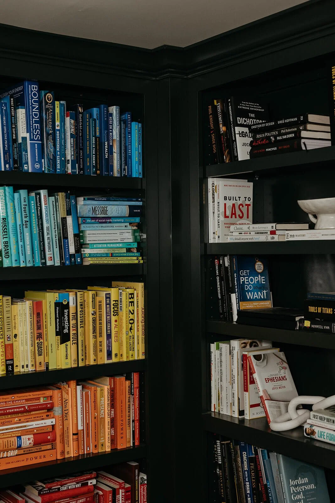 Close-up of a built-in bookshelf painted in a dark, rich color and styled with books organized by color, creating a rainbow effect.