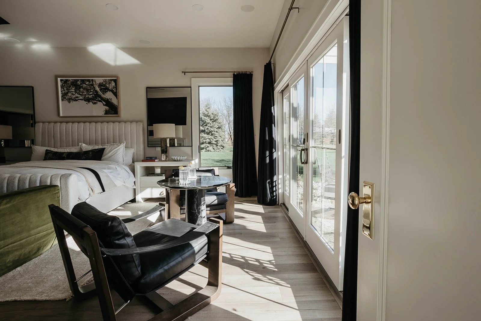 Master bedroom sitting area with a dark leather armchair, round marble-top side table, and large sliding doors leading to an outdoor deck, providing a view of the yard.