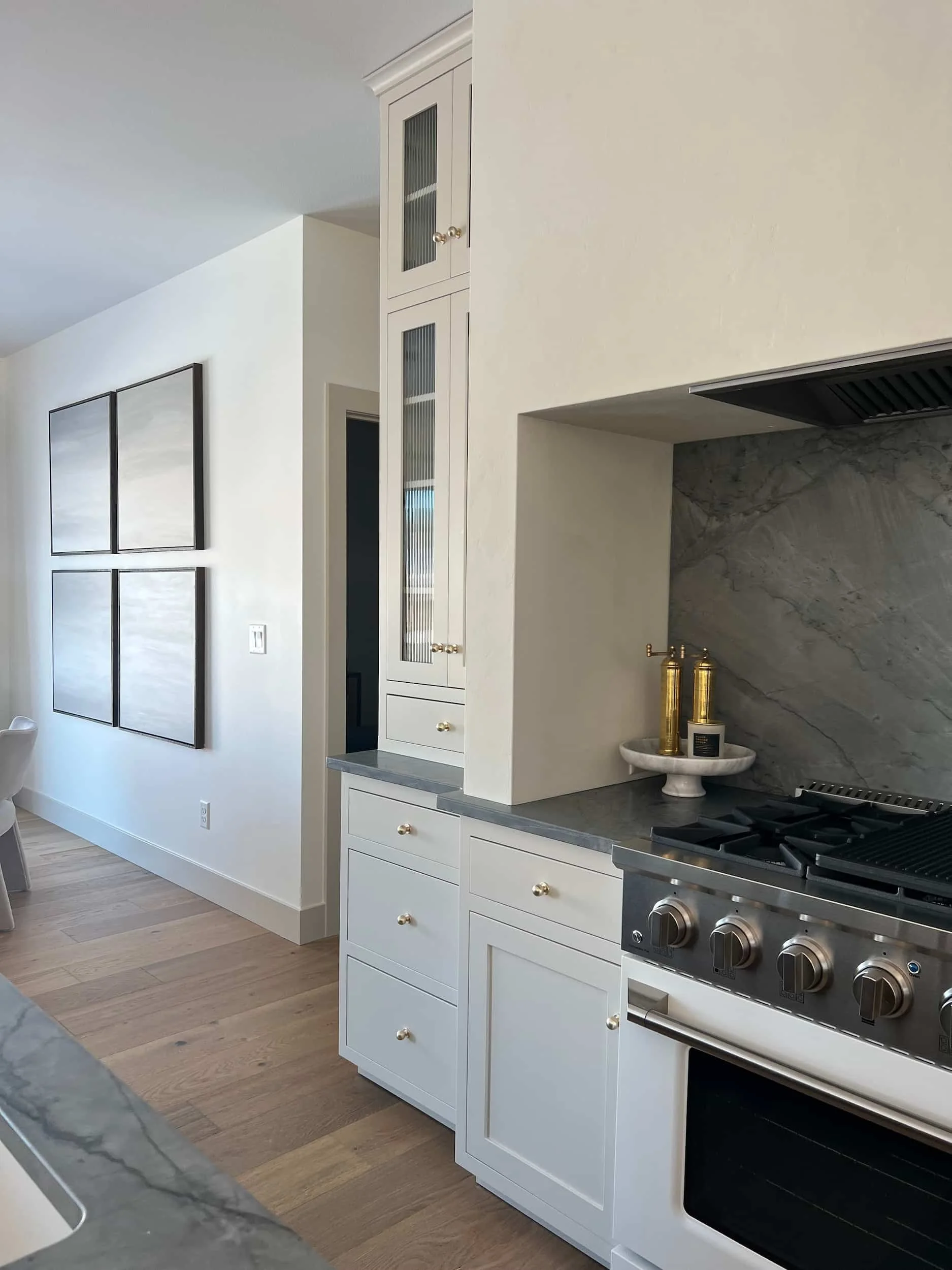 Kitchen perspective showing the stove, soapstone counters, and a built-in cabinet. Four square framed black and white artworks are visible on the side wall.
