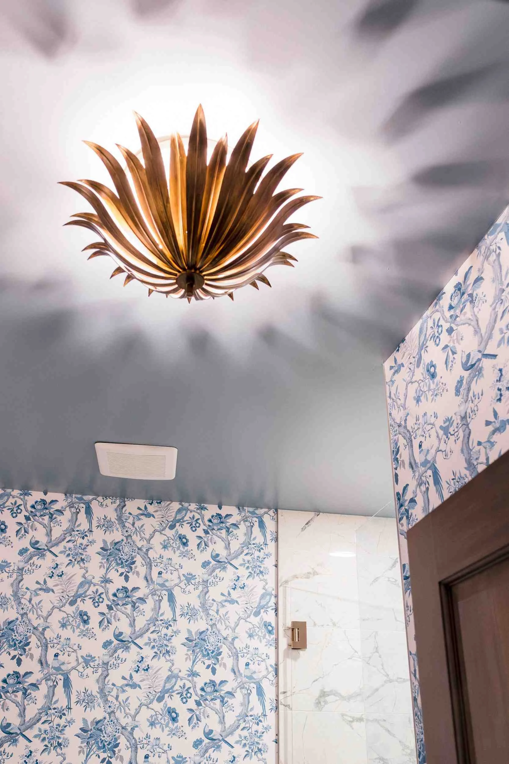 Close-up of a striking gold lotus-leaf flush mount light fixture against a light blue ceiling, casting starburst shadows.