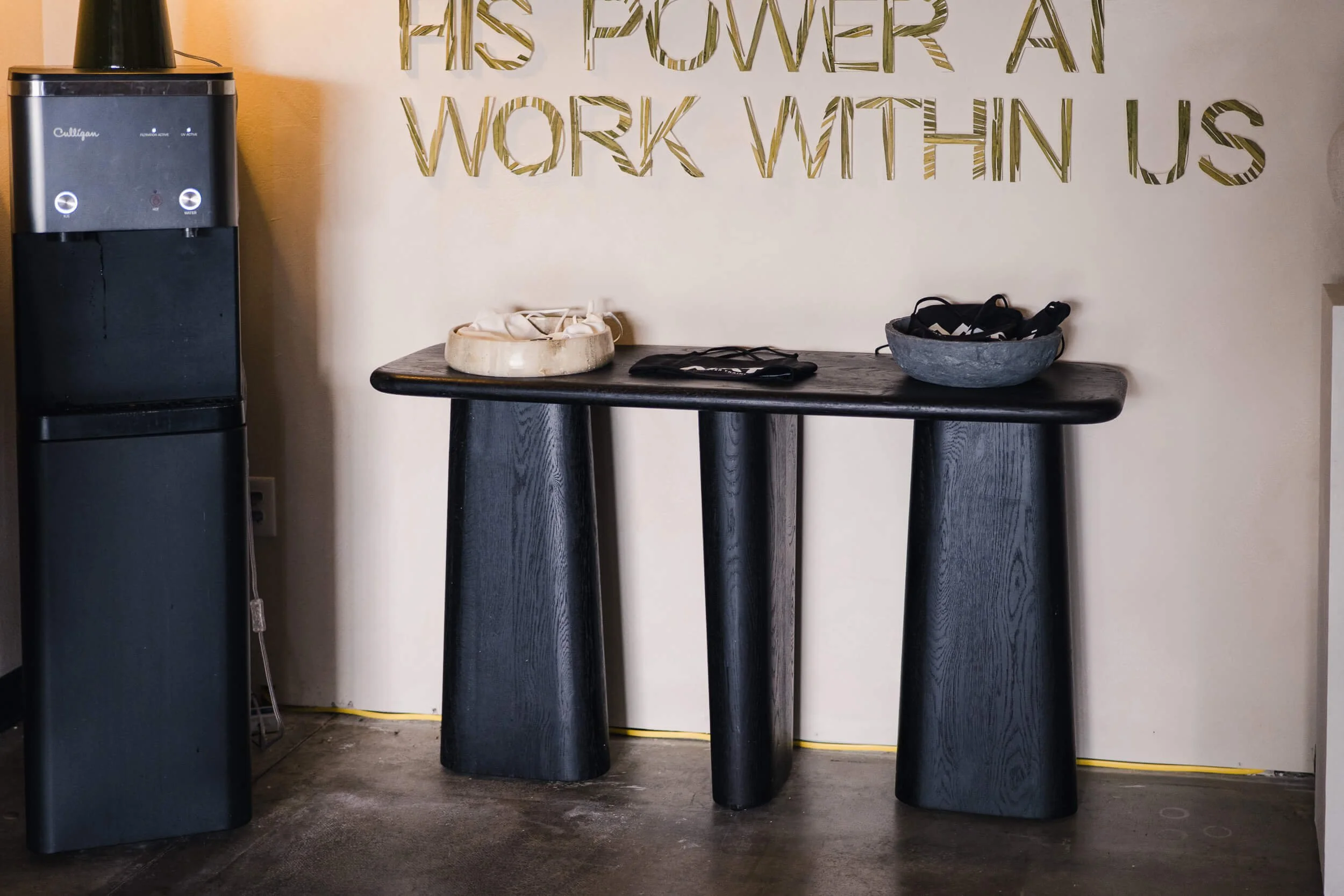 Small black console table styled with black bowls, set against a light, textured wall below the main wall art text