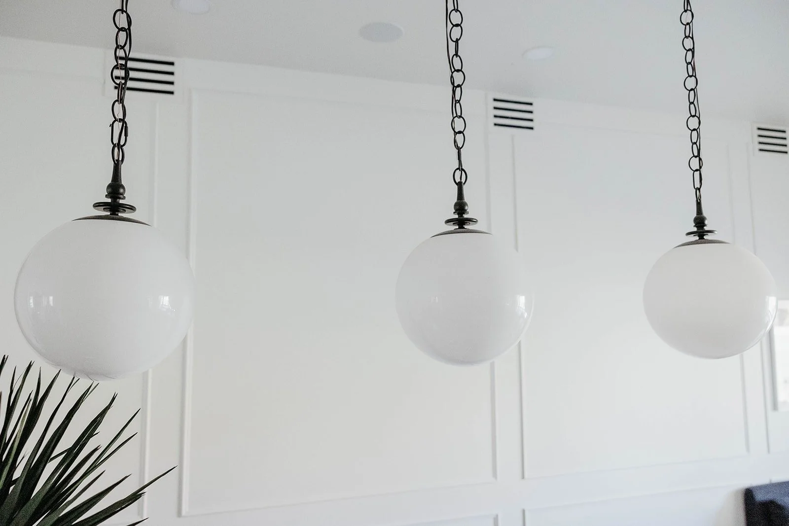 Detail of three large white globe pendant lights hanging from black chains against a clean white paneled ceiling.
