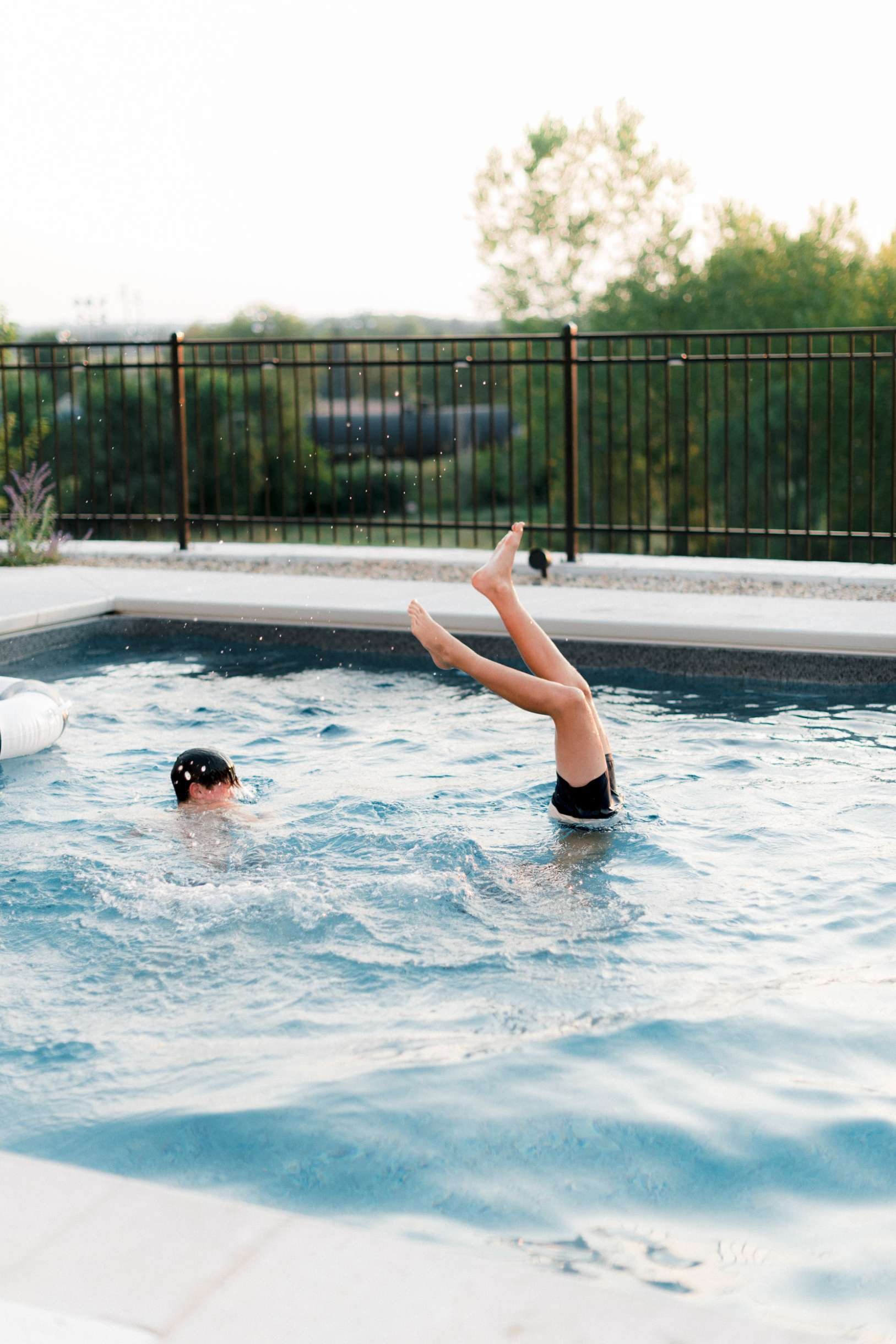 Child doing a handstand in the pool water near the edge, with sunlight reflecting off the surface.
